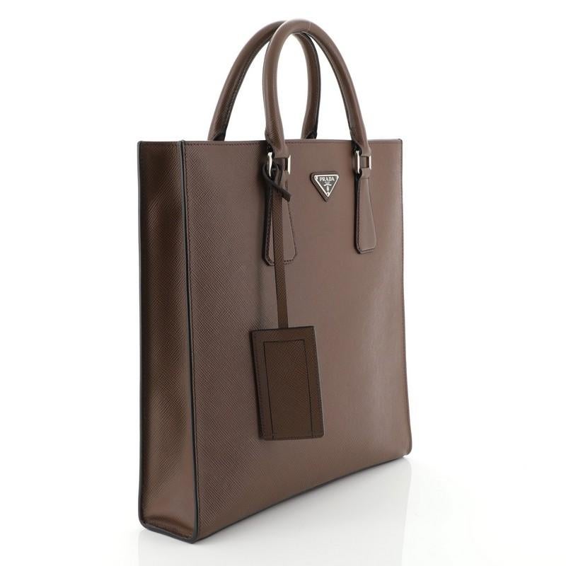 This Prada Open Tote Saffiano Leather North South, crafted from brown saffiano leather, features dual rolled leather handles, raised Prada logo, and silver-tone hardware. Its zip closure opens to a black leather interior with side zip and slip