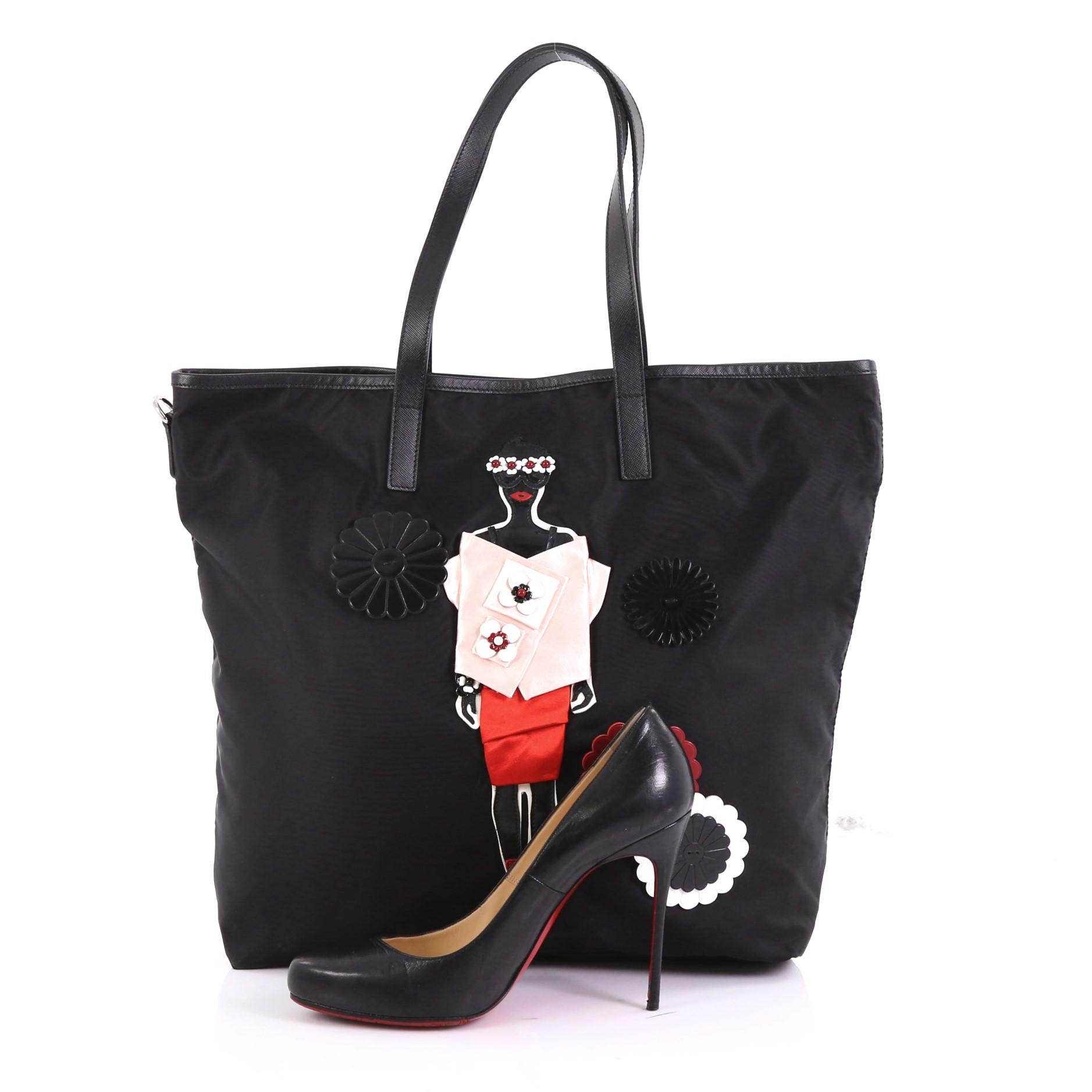 This Prada Open Tote Tessuto with Applique Large, crafted in black tessuto with applique, features dual flat leather handles and silver-tone hardware. Its wide open top showcases a black fabric interior with zip pocket. **Note: Shoe photographed is