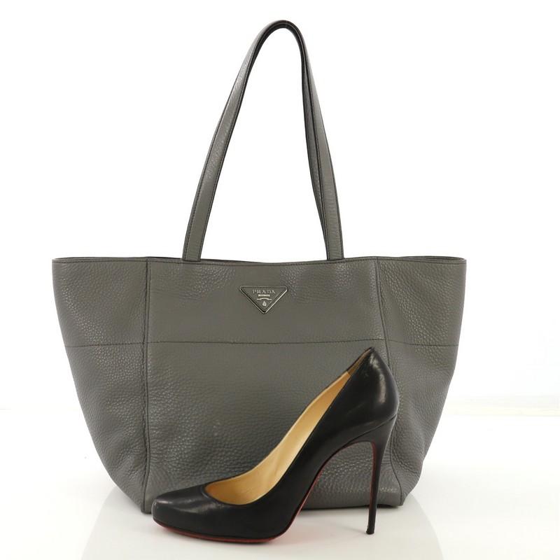This Prada Open Tote Vitello Daino Small, crafted from gray vitello daino leather, features dual flat leather handles and silver-tone hardware. Its hidden magnetic snap closure opens to a light beige fabric interior with side zip pockets. **Note: