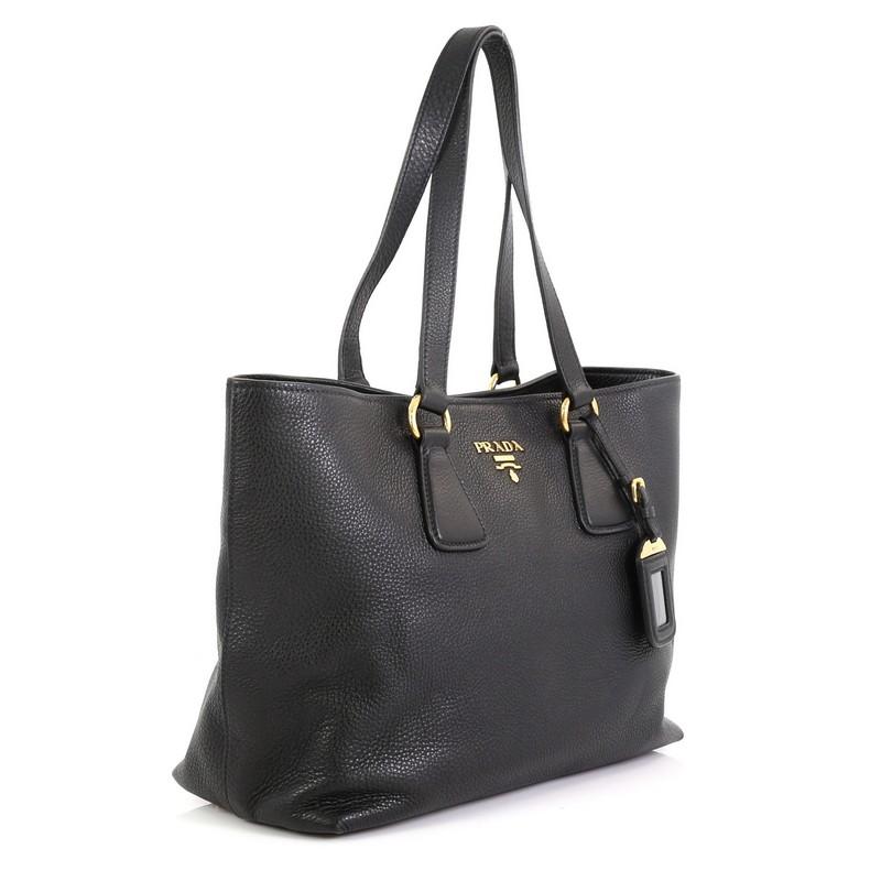 This Prada Open Tote Vitello Daino Small, crafted from black vitello daino leather, features dual flat leather handles and gold-tone hardware. Its magnetic snap button closure opens to a black fabric interior with side zip and slip pockets.