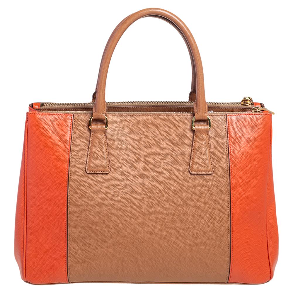 Loved for its classic appeal and functional design, the Galleria tote is one of the most iconic and popular bags from the house of Prada. This beauty in orange and beige is crafted from Saffiano lux leather and is equipped with two top handles and