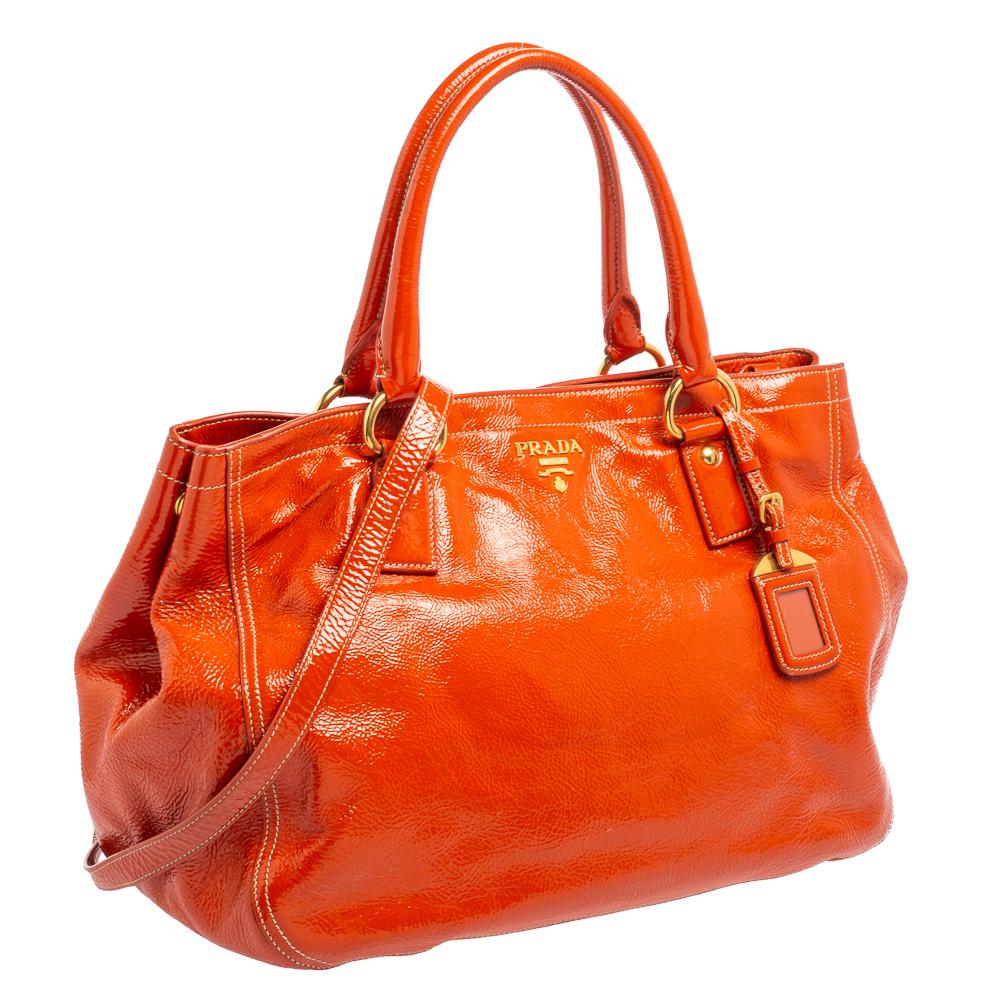 Easy to carry and stylish in appearance, this shopping tote from the House of Prada will certainly be your favorite pick for the season. It is crafted using orange patent leather, with a gold-tone logo perched on the front. This tote provides two