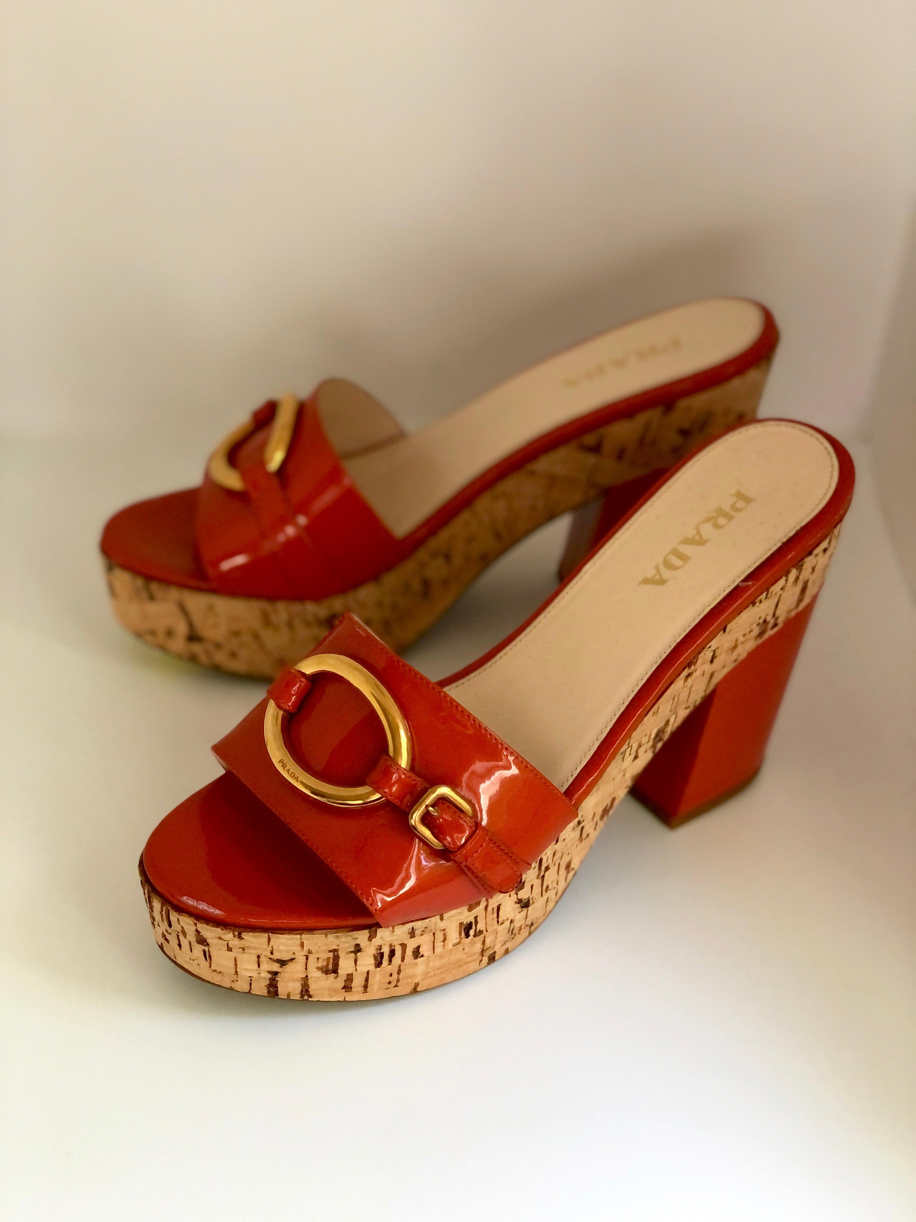 Offered is a pair of Miuccia Prada orange patent leather with cork platform and chunky medium heel slide / sandal.  The Prada slide / sandal has a gold metal ring on top engraved 