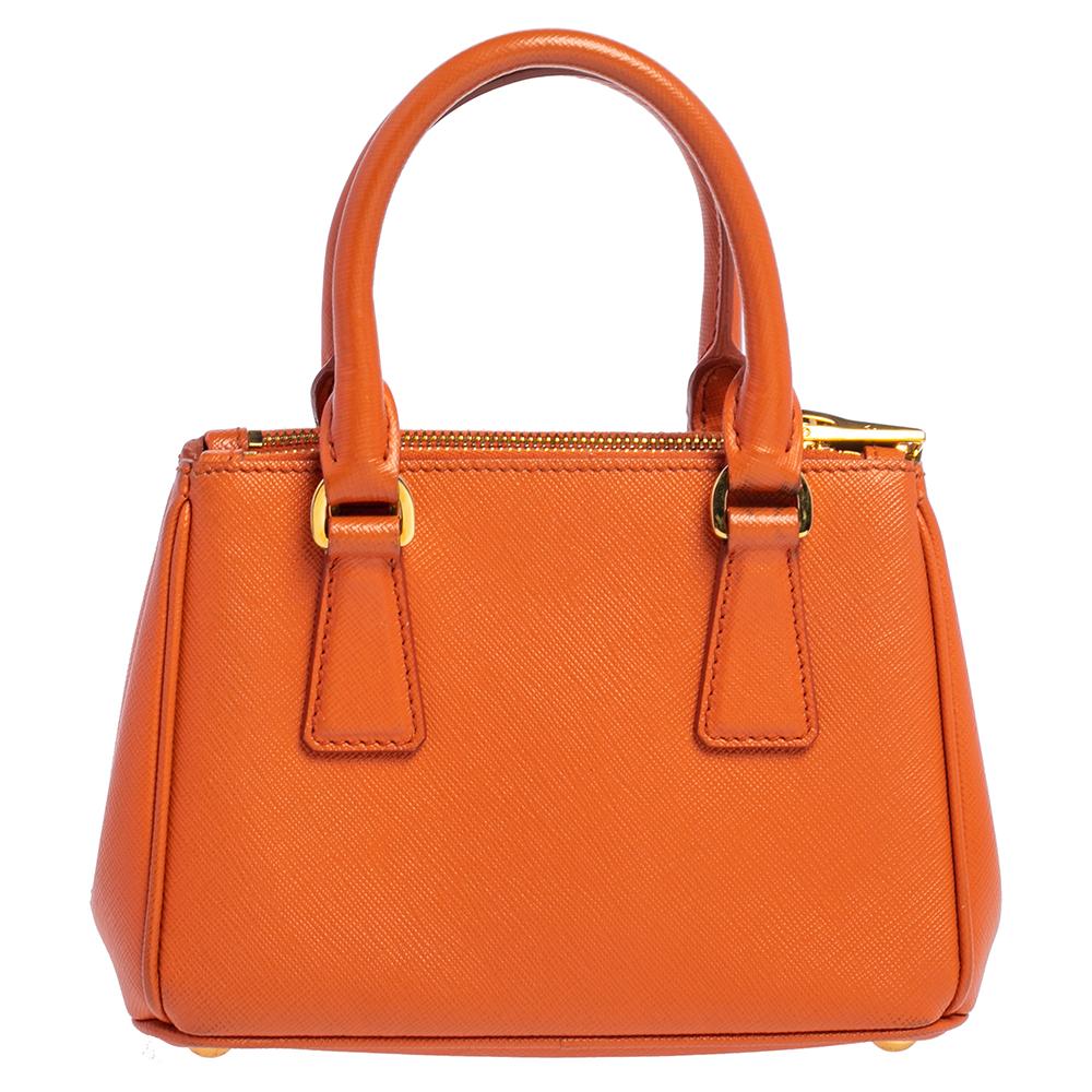This classy and sophisticated tote from Prada is a must-have! Crafted in orange Saffiano leather, it comes with double top handles, an adjustable shoulder strap, and a leather clochette. An orange and gold-tone brand plaque adorns the front. It