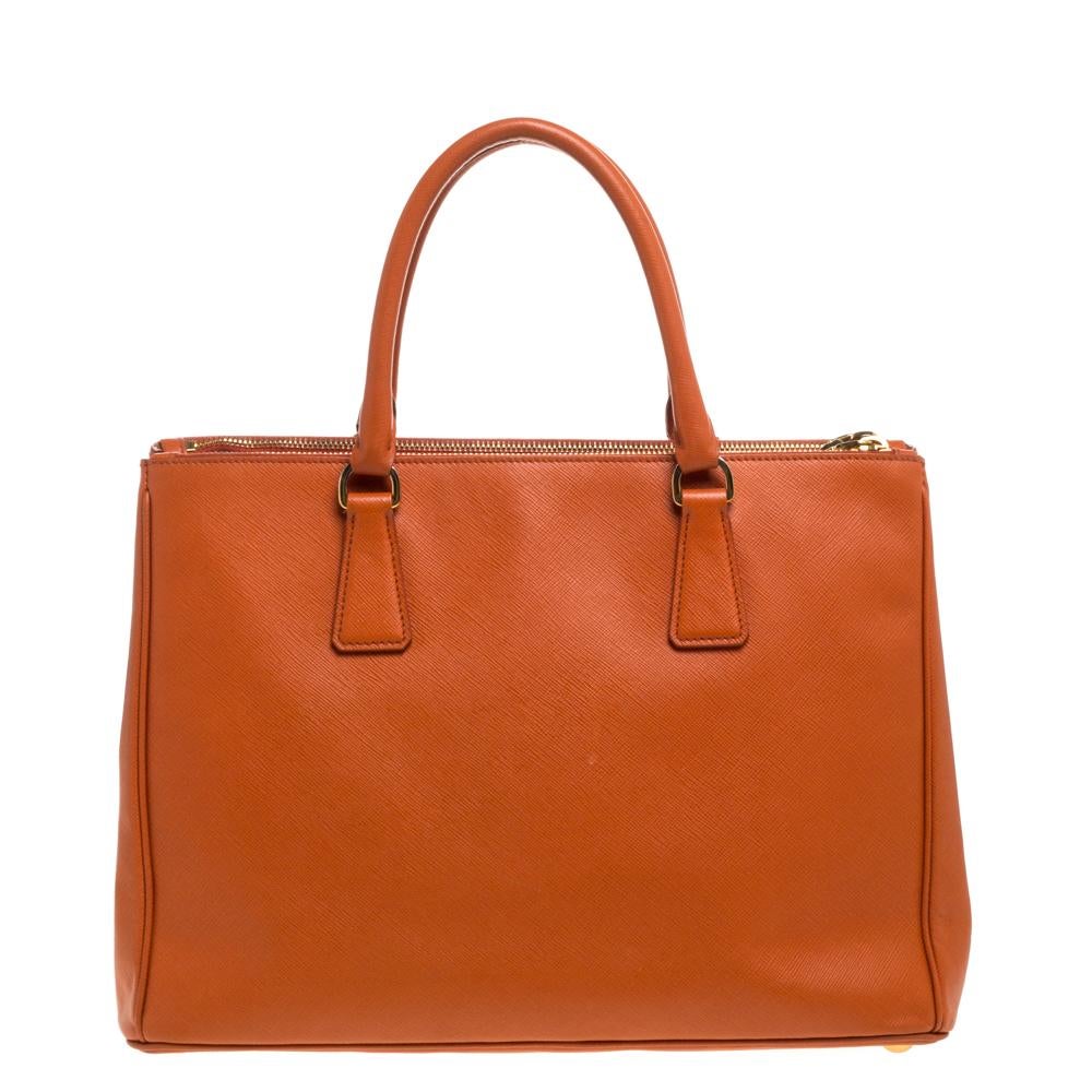 Feminine in shape and grand on design, this Double Zip tote by Prada will be a loved addition to your closet. It has been crafted from Saffiano Lux leather and styled minimally with gold-tone hardware. It comes with two top handles, two zip