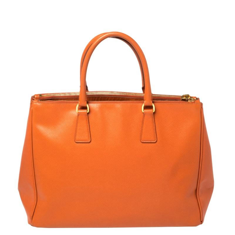 Feminine in shape and grand on design, this Double Zip tote by Prada will be a loved addition to your closet. It has been crafted from Saffiano Lux leather in an orange hue and styled minimally with gold-tone hardware. It comes with two top handles,