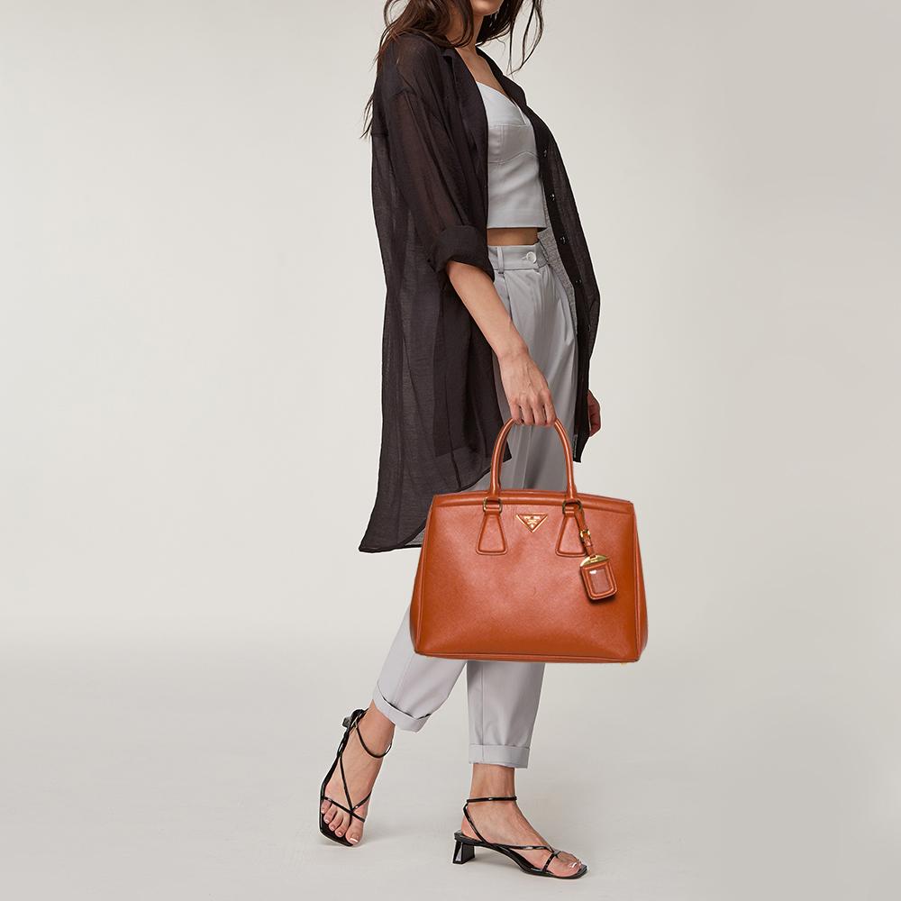 Meticulously created, this Parabole tote by Prada is a style statement in itself. Designed from Saffiano Lux leather into a sturdy shape, it exudes style and class in equal measures. This delightful orange-hued piece is held by two top handles and