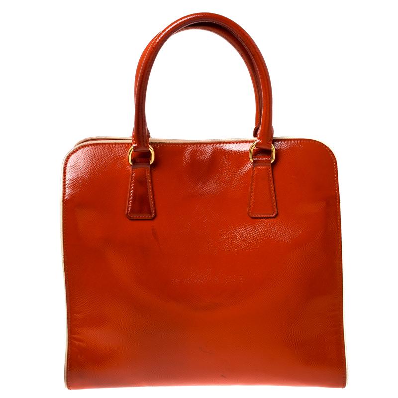 Giving satchels an elegant update, this bag by Prada will be a valuable addition to your closet. It has been crafted from orange Saffiano leather into a structured silhouette with gold-tone metal outlines. It comes with dual top handles, a
