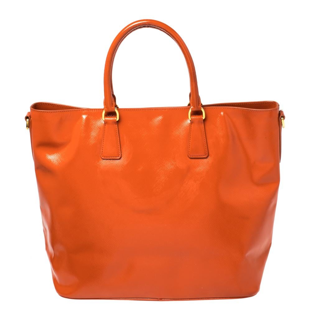 Turn heads when you go out carrying this beautifully crafted bag from Prada. Carry this orange bag to your next event for a statement-making impression. It is crafted from Saffiano Patent leather and is styled with dual handles, a shoulder strap,