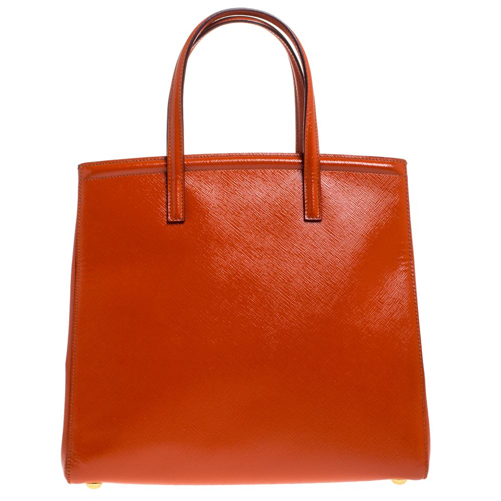 Masterfully created, this Prada tote is a style icon. Designed in a Saffiano Vernice leather body, it exudes style and class in equal measures. This delightful orange piece is held by two top handles and equipped with a spacious fabric