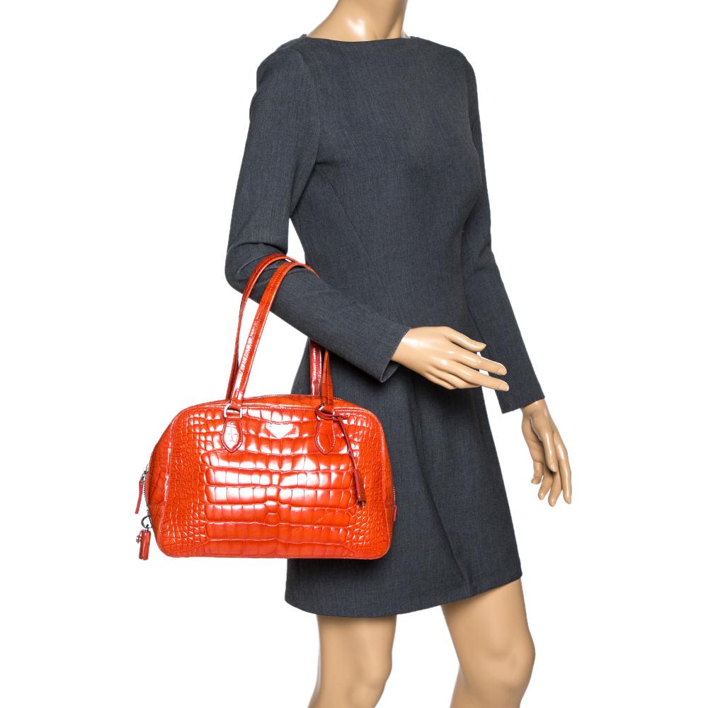 This elegant Bauletto bag from Prada is crafted from shiny croc-embossed leather and is perfect for your fashionable outings. The beautiful orange color is ravishing. The bag features splendid details in the form of dual top handles, a detachable