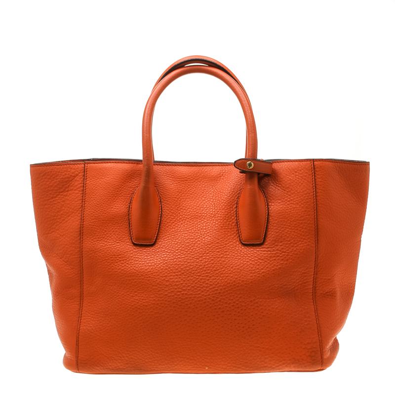 This shopper tote from Prada is a timeless piece. The bag comes in a luxurious orange leather exterior with gold-tone hardware. It features double top handles, a removable shoulder strap and protective metal feet at the bottom. The nylon lined