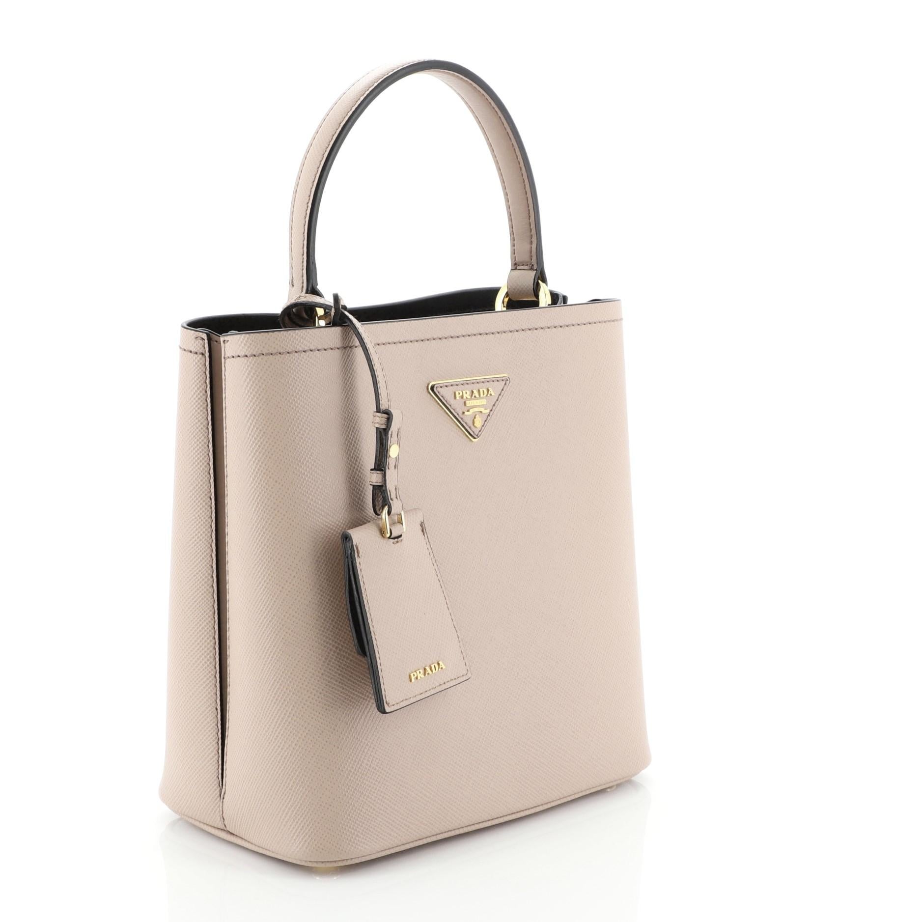 This Prada Panier Bucket Bag Saffiano Leather Medium, crafted in pink saffiano leather, features a leather top handle and gold- tone hardware. Its wide open top showcases a black leather interior divided into two compartments. 

Condition: