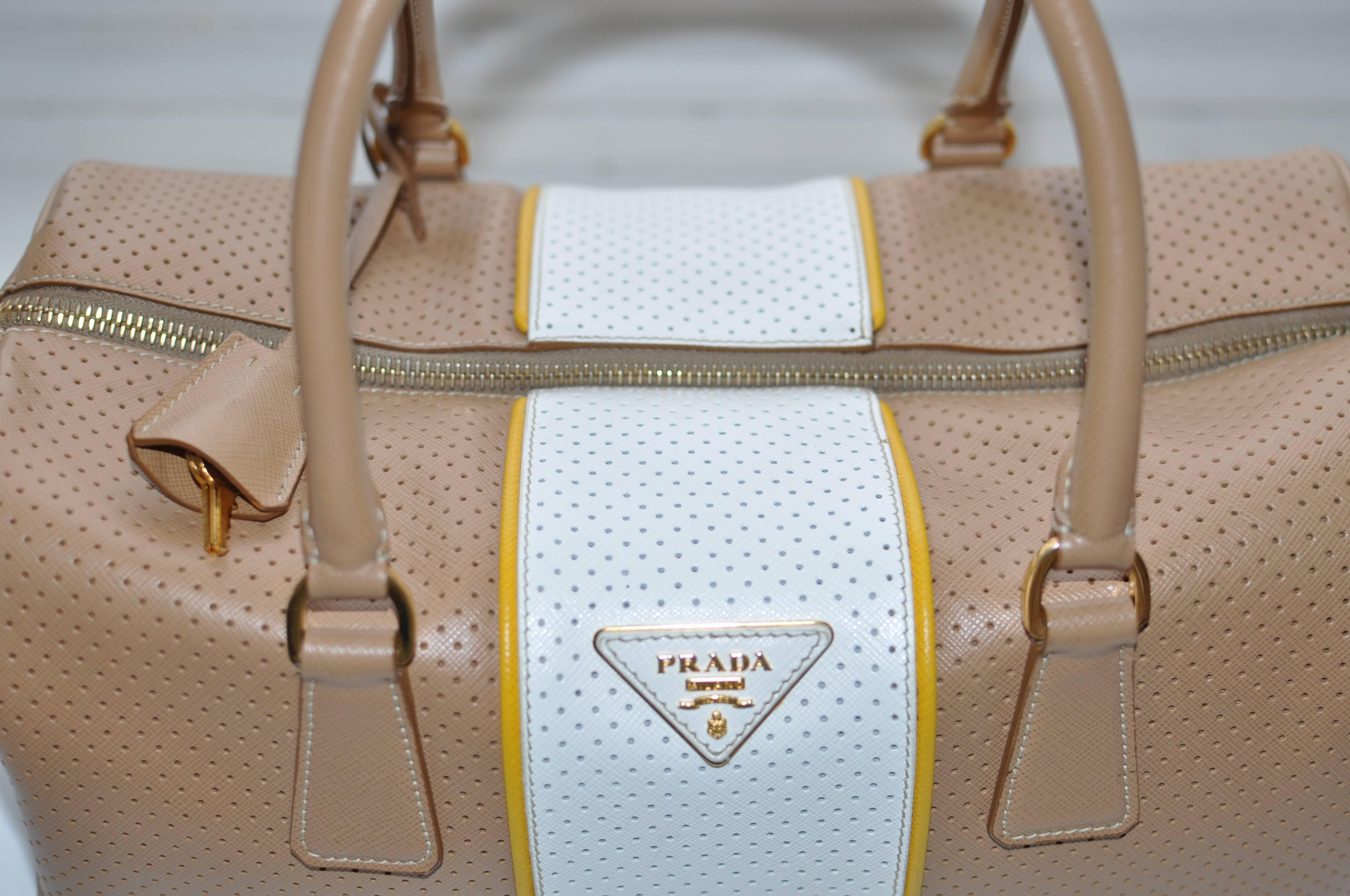 This white and beige perforated leather handbag has yellow stripping on either side the white band; nice gold colored hardware, including half moon raised feet; keys; lock and a dust bag. The interior is gold Prada logo with the Prada plaque on the