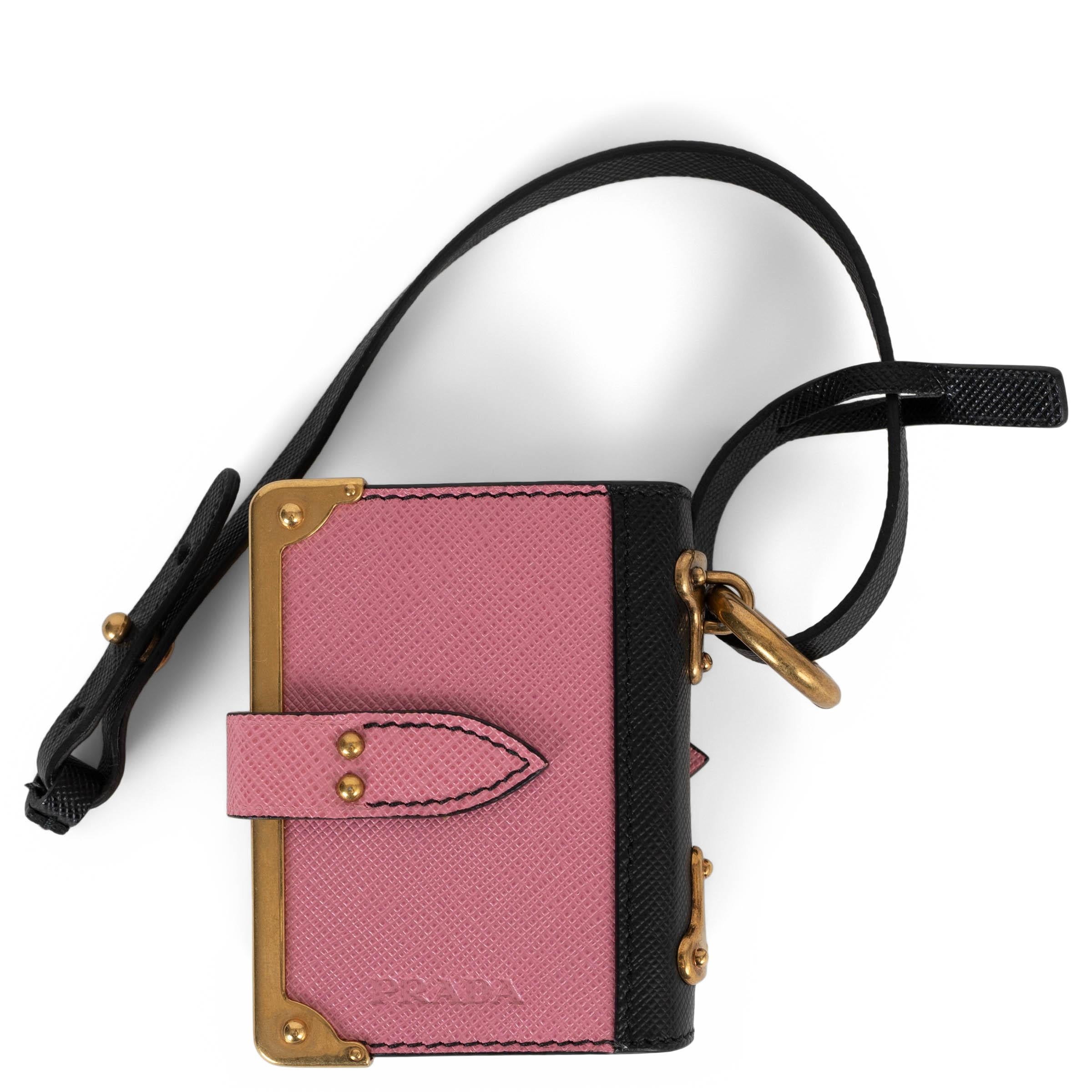 This 100% authentic Prada Cahier bag charm is crafted in pink and black Saffiano leather, styled like a miniature notebook. It opens to reveal blank pages secured by a gold-tone pin and features a coordinating leather strap. Antique gold-tone metal
