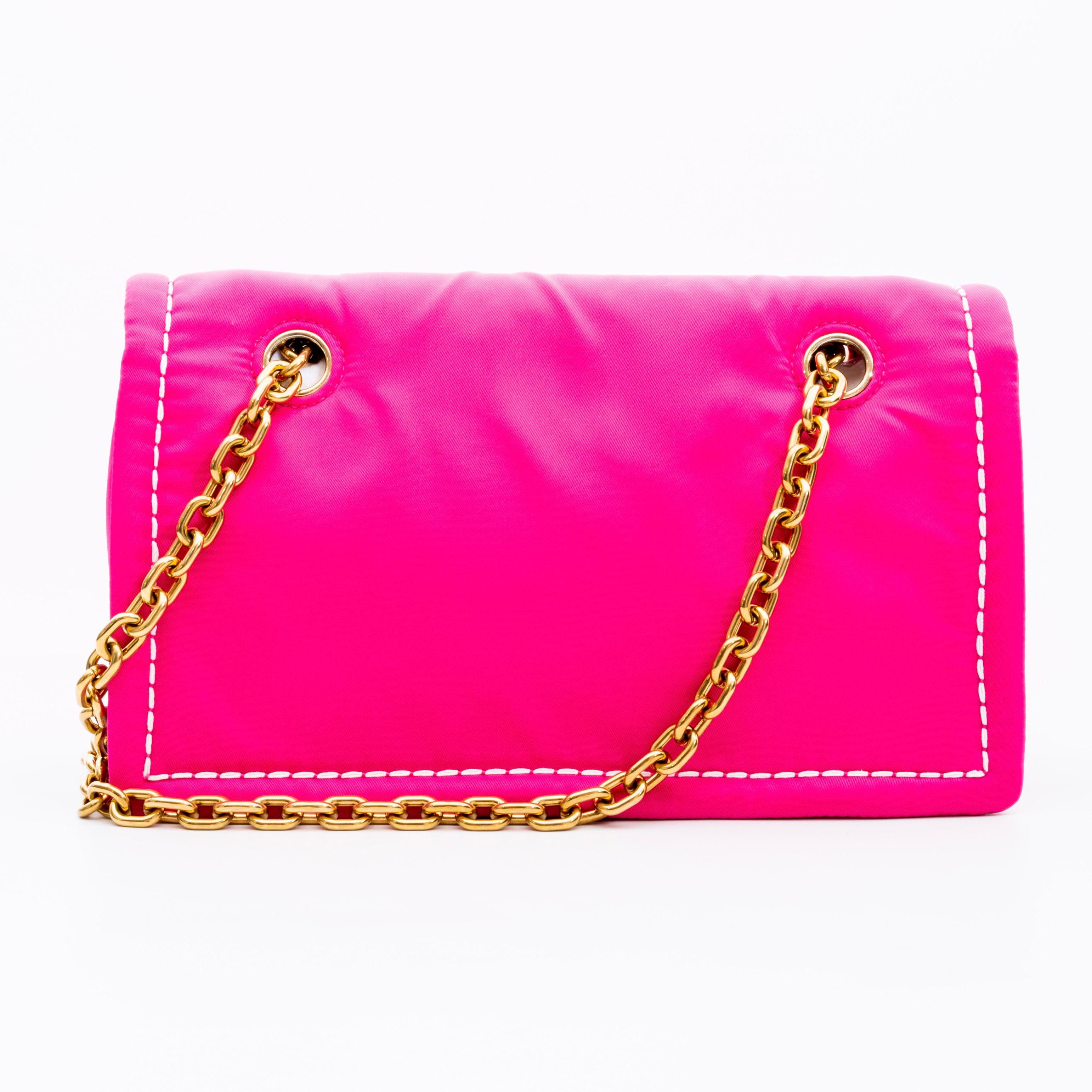 This bag is made with pink nylon and features white contrasting stitching, gold tone hardware, a front logo plaque, shoulder pad and a matching interior in pink with a zip pocket.

COLOR: Pink
MATERIAL: Nylon
ITEM CODE: 25
MEASURES: H 6.5” x L 10” x