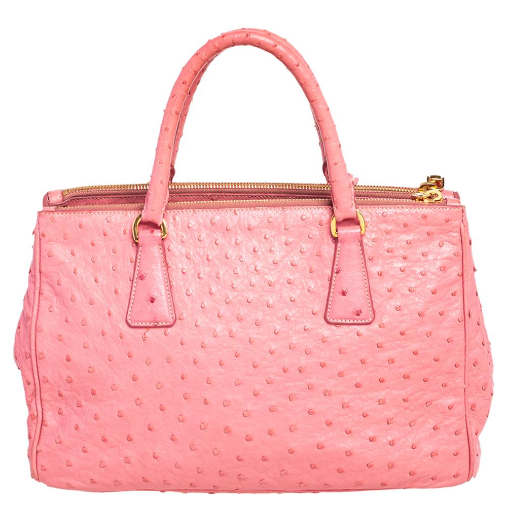 Loved for its classic appeal and functional design, Galleria is one of the most iconic and popular bags from the house of Prada. This beauty in pink is crafted from Ostrich leather and is equipped with two top handles, the brand logo at the side,