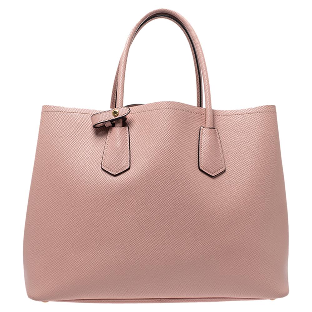 Diese elegante Tote von Prada ist aus Leder gefertigt und eignet sich perfekt für den täglichen Gebrauch. Die Tasche verfügt über doppelte Griffe:: schützende Metallfüße und ein Lederschild auf der Vorderseite. Die Tasche öffnet sich zu einem