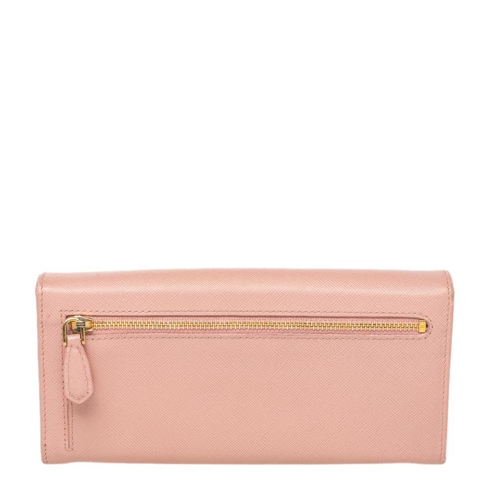 Made of elegant Saffiano leather in pink, this wallet from Prada is beautified with bow detail on the front flap. The flap opens to a sleek interior featuring open compartments, multiple card slots, and a zipped pocket. This wallet comes with a