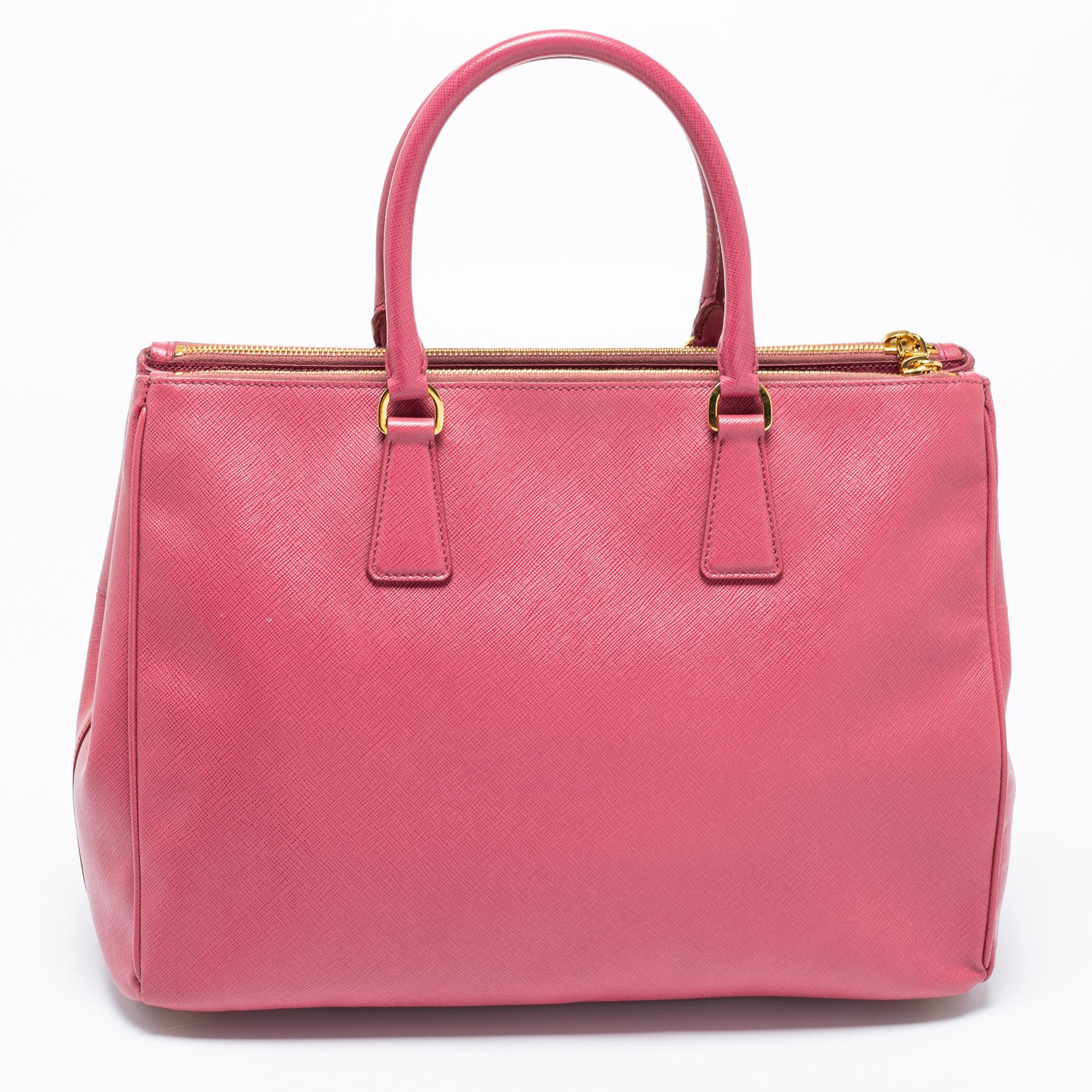 This Double Zip tote by Prada will be a loved addition to your closet. It has been crafted from pink Saffiano Lux leather and added with gold-tone hardware, two top handles, and nylon compartments. The bag is complete with protective metal feet and