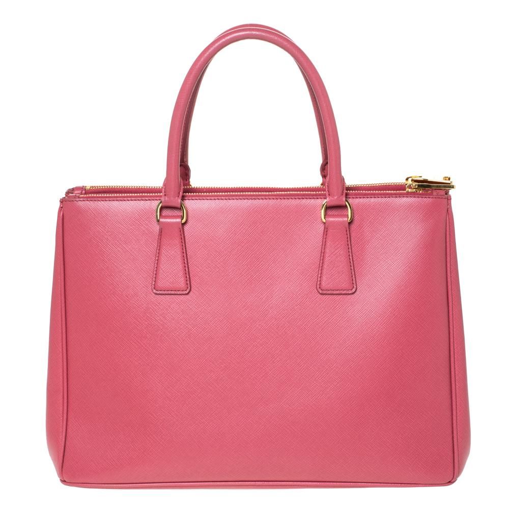 Feminine in shape and grand on design, this Double Zip tote by Prada will be a loved addition to your closet. It has been crafted from pink Saffiano Lux leather and styled minimally with silver-tone hardware. It comes with two top handles, two zip
