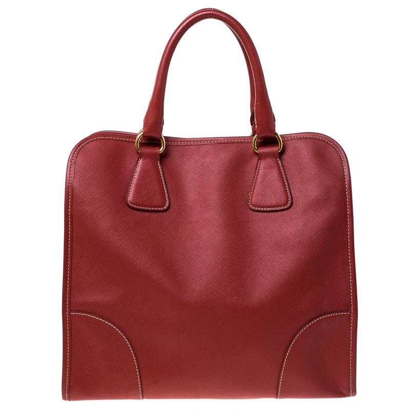 Flaunt an awesome style when you step out swaying this Prada satchel. It has been crafted from red Saffiano leather and held by two handles. The bag has a snap button that leads to a nylon interior equipped with pockets. Flaunting a structured body,