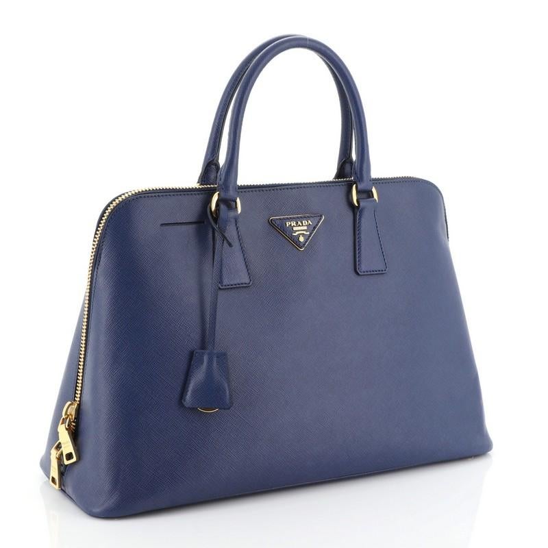 This Prada Promenade Bag Saffiano Leather Large, crafted from blue saffiano leather, features dual rolled handles, protective base studs and gold-tone hardware. Its zip closure opens to a blue fabric interior with side zip and slip pockets.