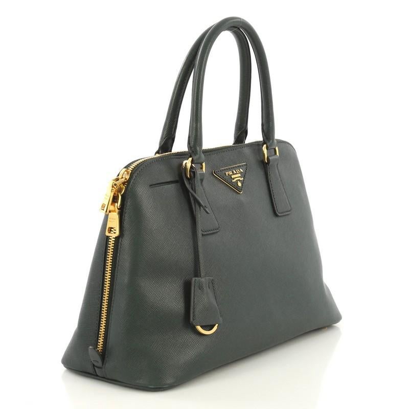 This Prada Promenade Bag Saffiano Leather Medium, crafted from green saffiano leather, features dual rolled handles, protective base studs and gold-tone hardware. Its zip closure opens to a black fabric and green leather interior divided into two
