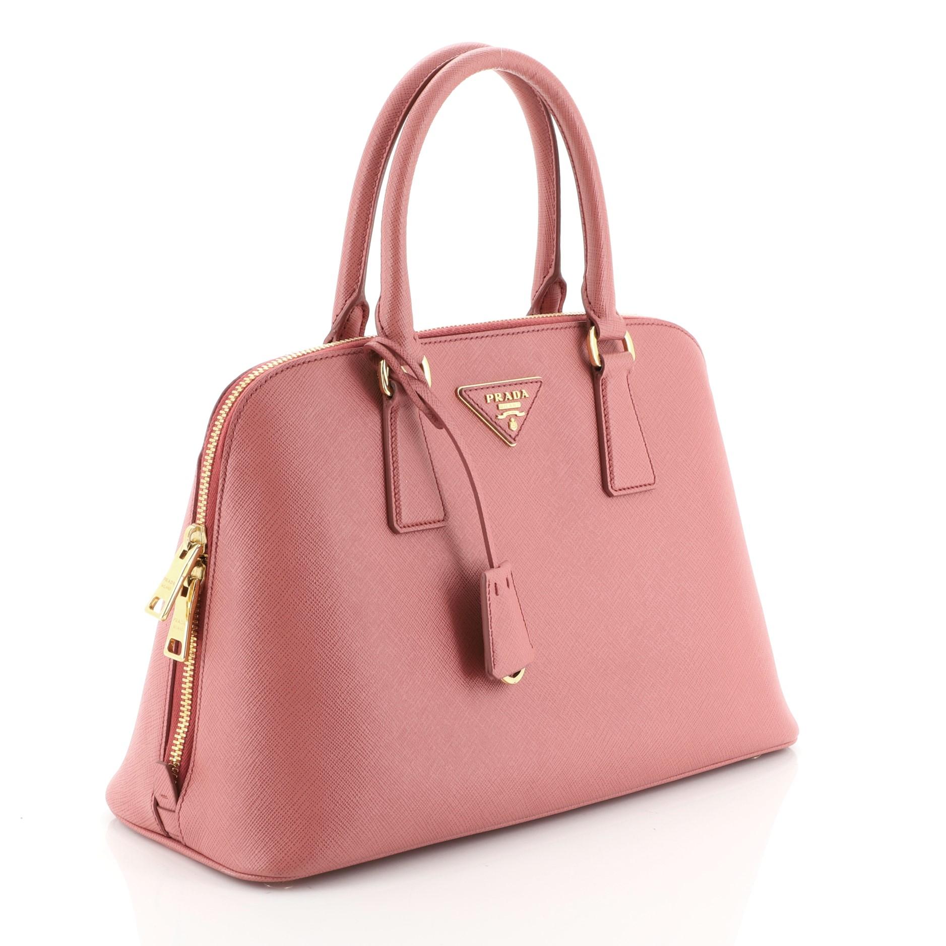This Prada Promenade Bag Saffiano Leather Medium, crafted from pink saffiano leather, features dual rolled handles, protective base studs and gold-tone hardware. Its zip closure opens to a pink leather and fabric interior divided into two