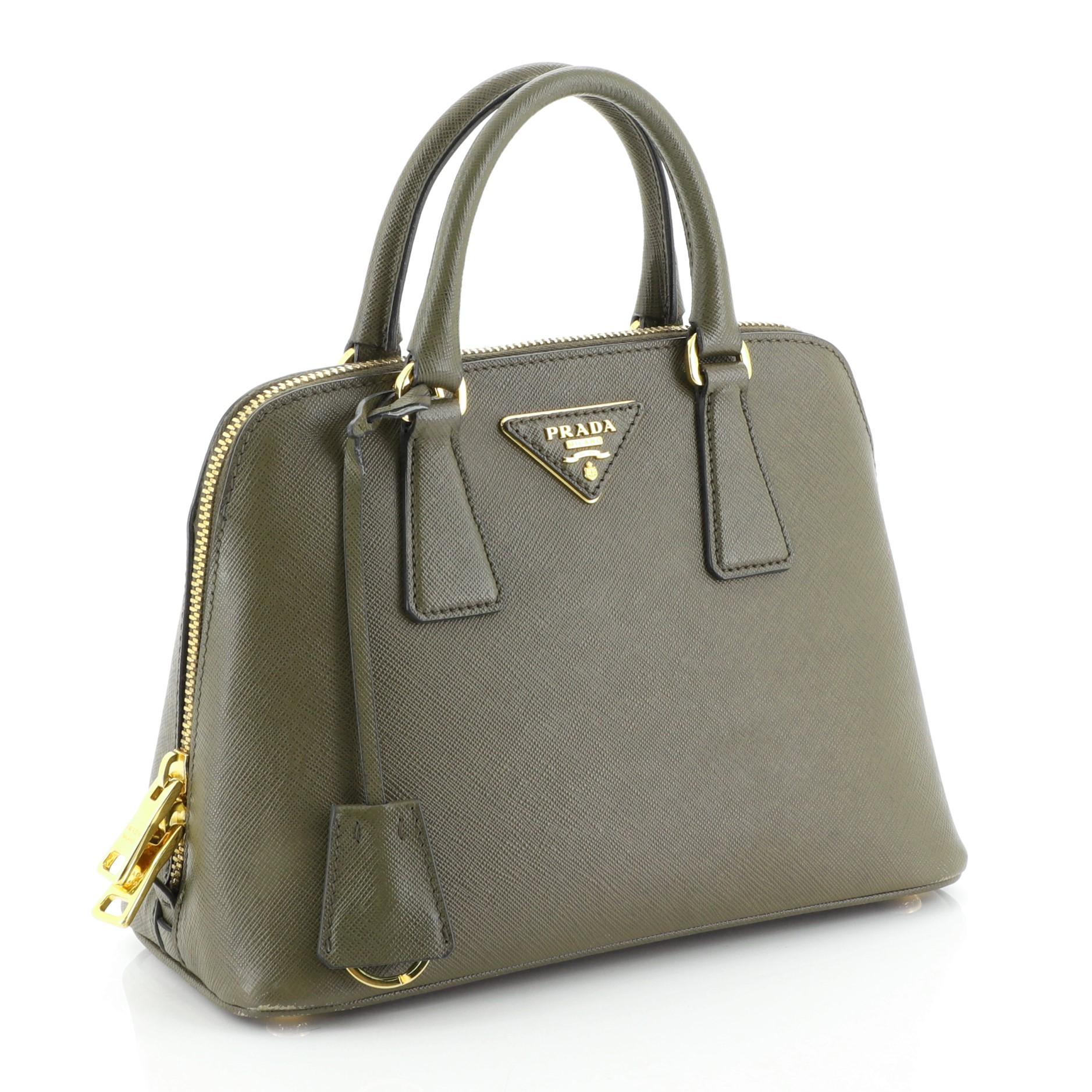 This Prada Promenade Bag Saffiano Leather Small, crafted from green saffiano leather, features dual rolled handles, triangle Prada logo, and gold-tone hardware. Its two-way zip closure opens to a black fabric interior with a center zip compartment