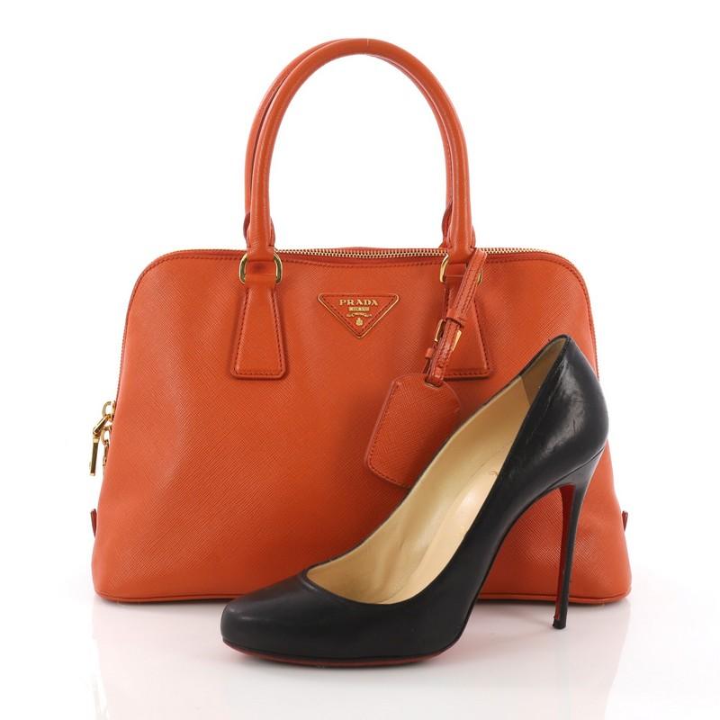 This Prada Promenade Handbag Saffiano Leather Medium, crafted from orange saffiano leather, features dual rolled handles, protective base studs and gold-tone hardware. Its zip closure opens to an orange fabric interior divided into two compartments
