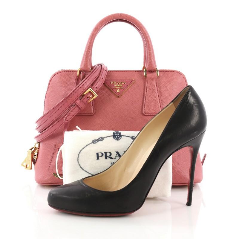 This Prada Promenade Handbag Saffiano Leather Small, crafted from pink saffiano leather, features dual rolled handles, triangle Prada logo, and gold-tone hardware. Its two-way zip closure opens to a pink fabric interior with a center zip compartment