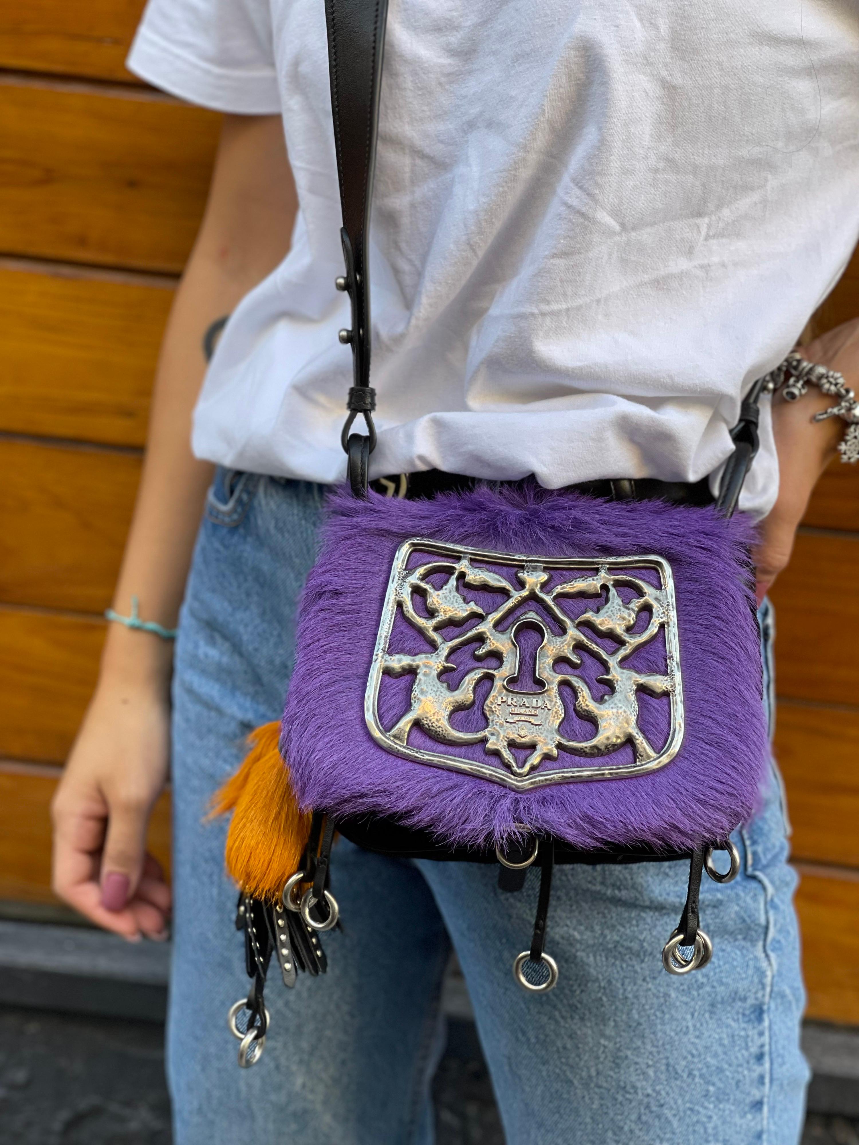 Prada Corsaire with  purple calf hair and black leather, with a touch of silver plated hardware. The bad has a black leather strap with some silver plated hardware. Inside the bag has 3 pockets made with black velvet and black leather. On the side,