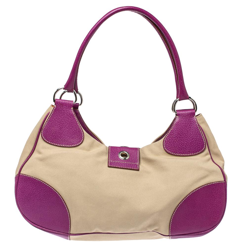 This stunning shoulder bag by Prada is stylish and perfect for day-outs with friends. Crafted from beige canvas and purple leather. It is styled with a front slender flap with buckle detailing, twin handles, silver-tone hardware, and a well-sized