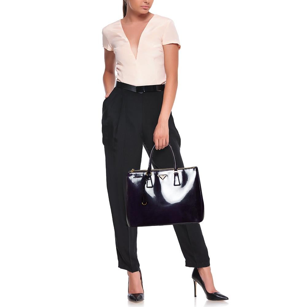 Feminine in shape and design, this Double Zip tote by Prada will be a loved addition to your closet. It is crafted from patent leather and styled minimally with gold-tone hardware. It comes with two top handles, two zip compartments, and a perfectly