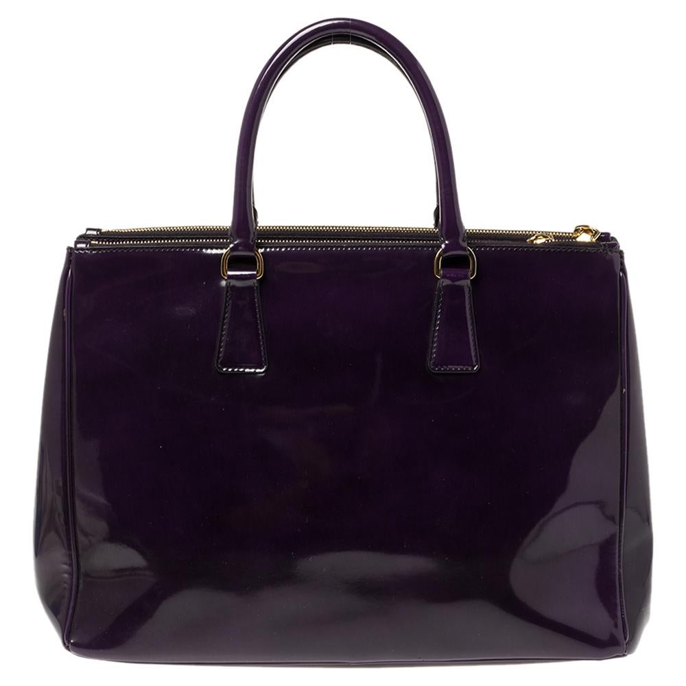 Feminine in shape and grand on design, this Double Zip tote by Prada will be a loved addition to your closet. It has been crafted from glossy patent leather in a purple hue and styled minimally with gold-tone hardware. It comes with two top handles,