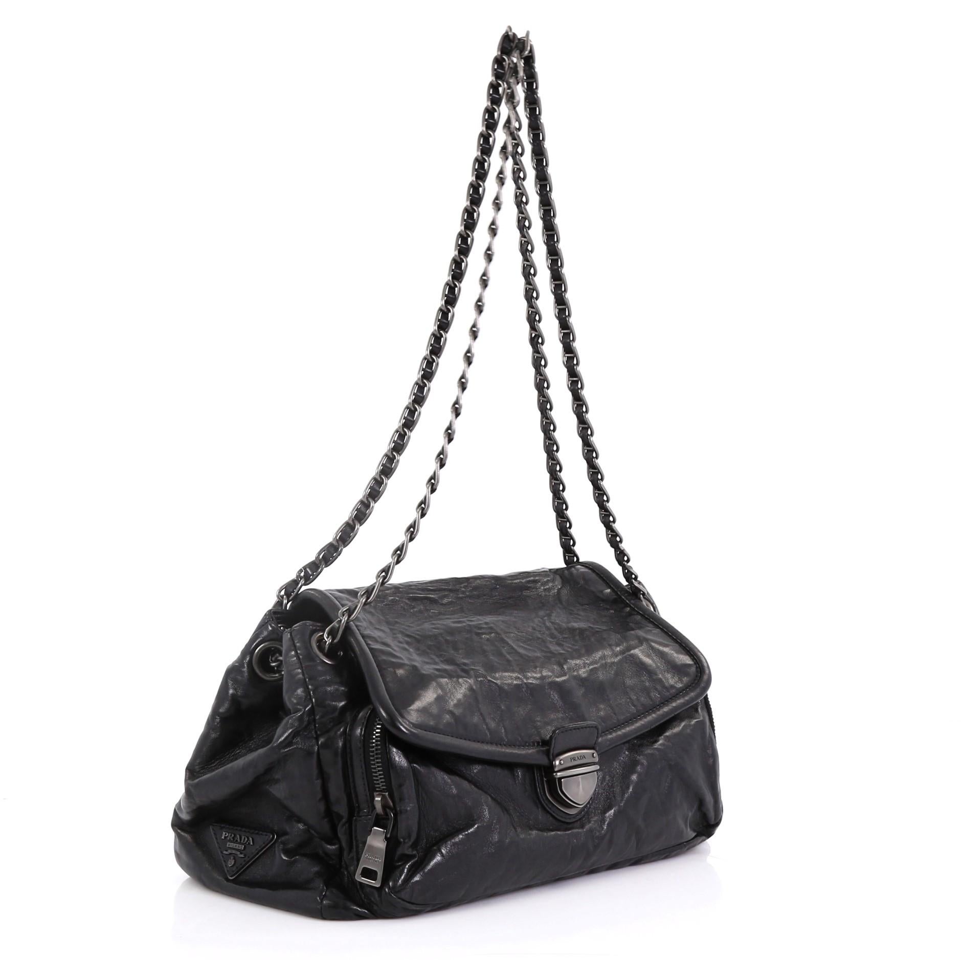This Prada Pushlock Chain Flap Shoulder Bag Nappa Antique Medium, crafted in black nappa antique, features woven-in leather chain straps, exterior back slip pocket, zip pocket under its flap, and matte gunmetal-tone hardware. Its push-lock closure