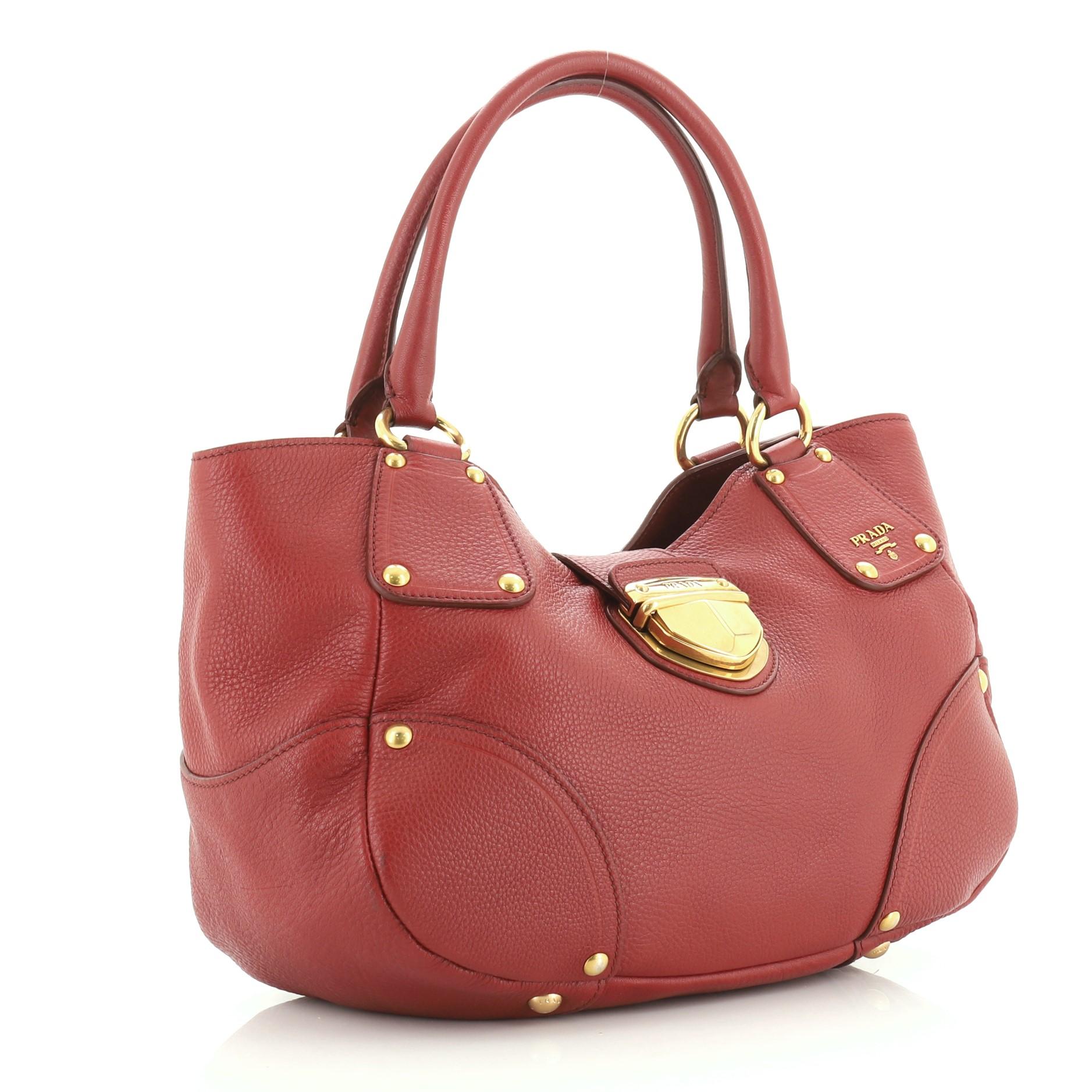 This Prada Pushlock Tote Vitello Daino Medium, crafted in red vitello daino leather, features dual rolled leather handles and gold-tone hardware. Its push-lock closure opens to a red fabric interior with zip and slip pockets. 

Estimated Retail