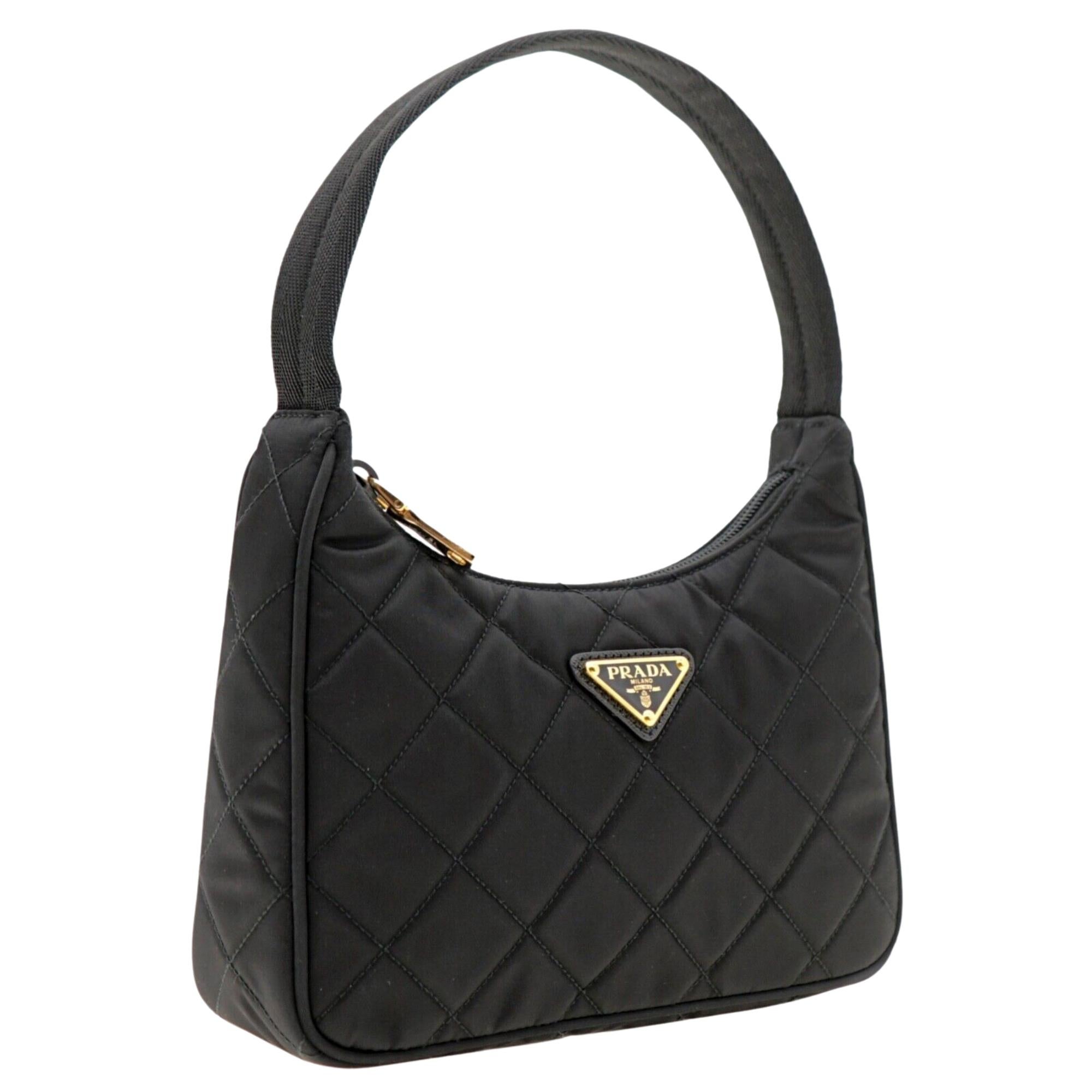 Questa mini borsa hobo di Prada è realizzata in nylon leggero trapuntato di colore nero e presenta una chiusura a zip, un manico superiore intrecciato ed è impreziosita dall'iconico logo a triangolo in metallo smaltato. Hardware color oro. Prada ref