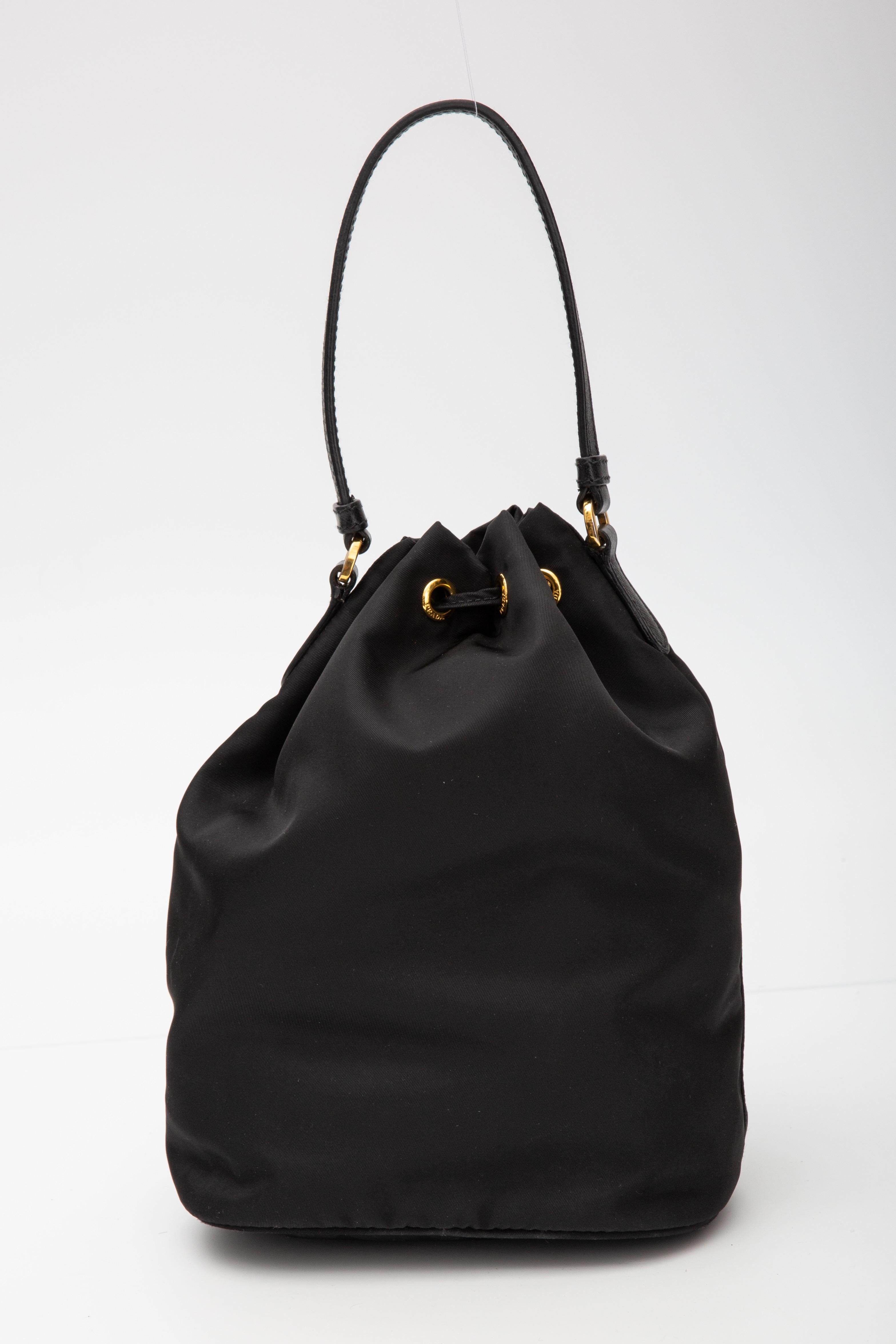 This Prada bag is made with black re-nylon and features gold tone hardware, drawstring closure, saffiano leather details, a leather adjustable and attachable shoulder strap, a front zip pocket and an open interior with logo jacquard woven fabric