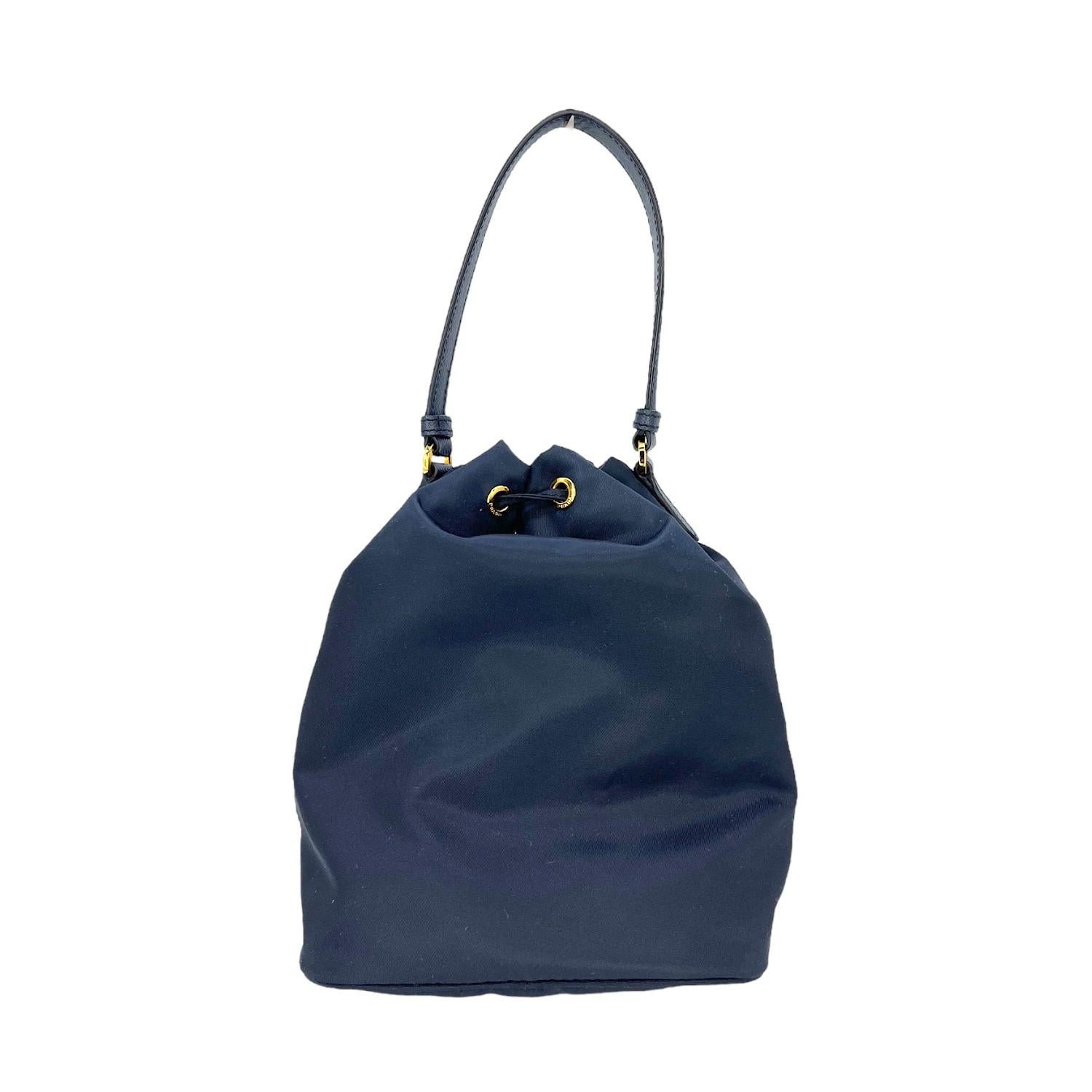 This Prada Re-Nylon Duet Bag was made in Italy and it is finely crafted in blue Re-Nylon exterior with gold-tone hardware features. It has a flat leather top handle. It comes with a removeable shoulder strap as well. It has a small frontal zipper