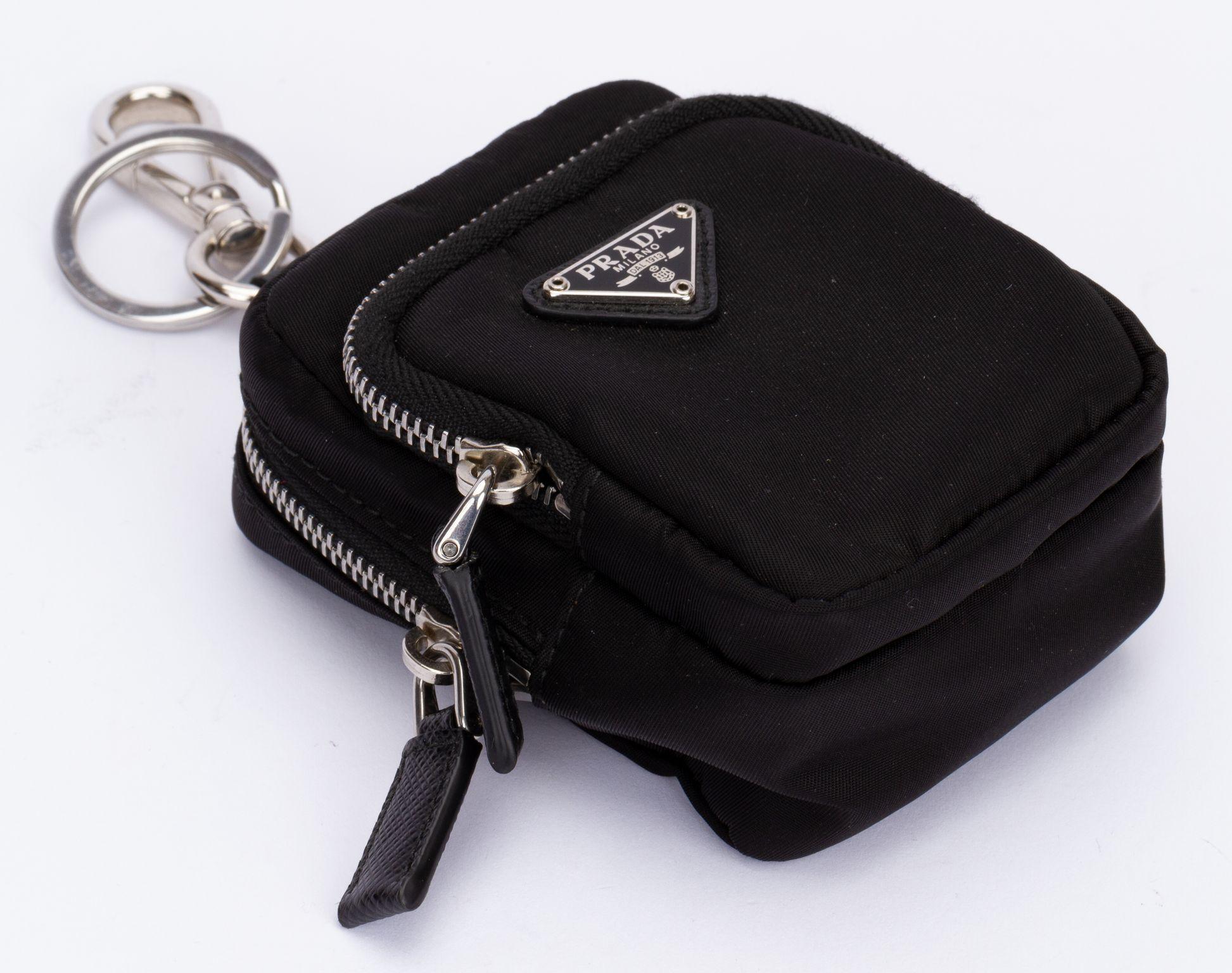 Prada Mini Pouch in black. The padded mini-pouch is made of Re-Nylon and from the latest Prada collection. It comes with a ring and a clip. It has two zipped compartments. On the front is a plate with the Prada logo on it.