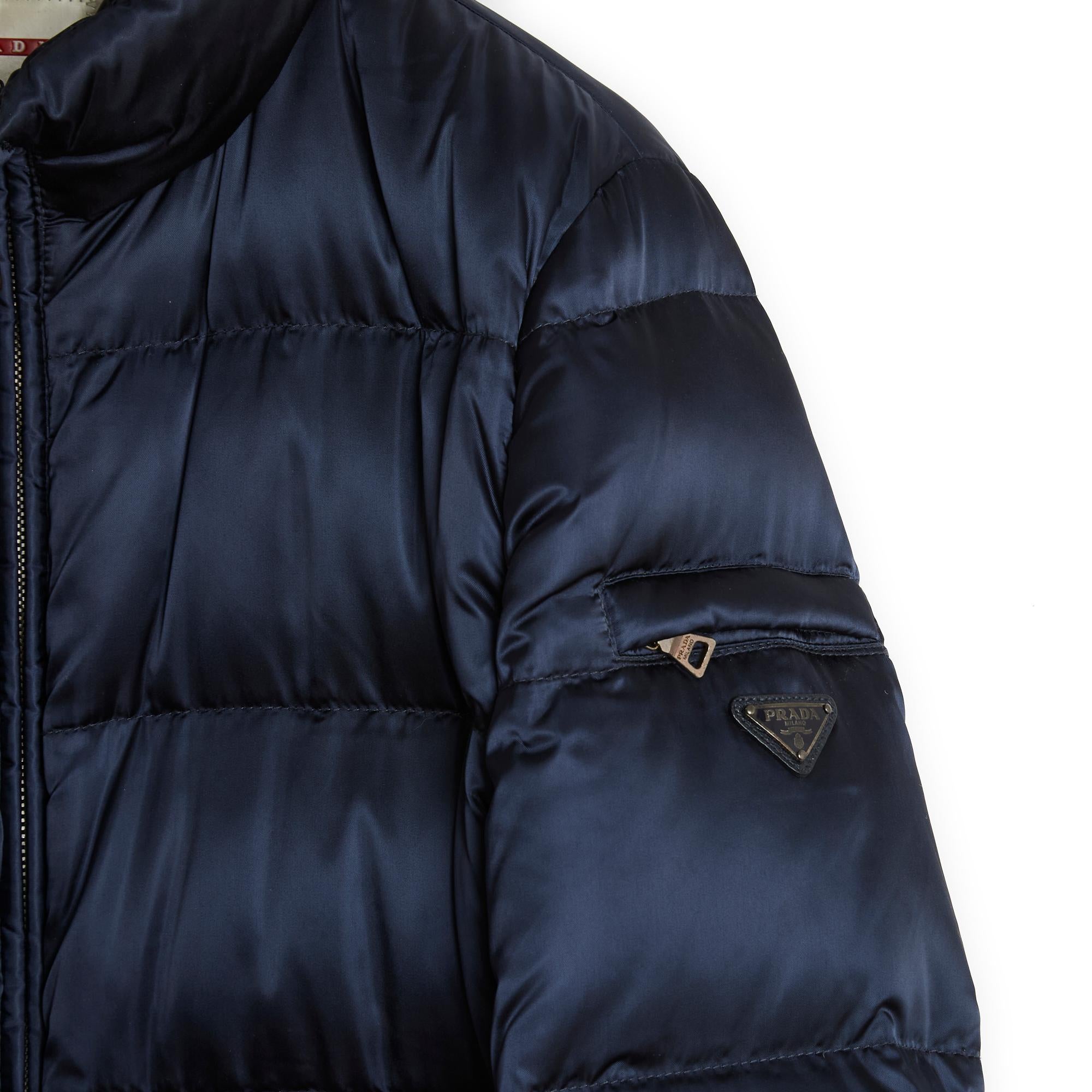 Prada coat, Re-Nylon style down jacket in navy blue satin polyamide and down, quilted, high collar closed all the way up with a long double-slider zip, long sleeves, one of which has a small zipped pocket and Prada logo, elastic at the wrist,