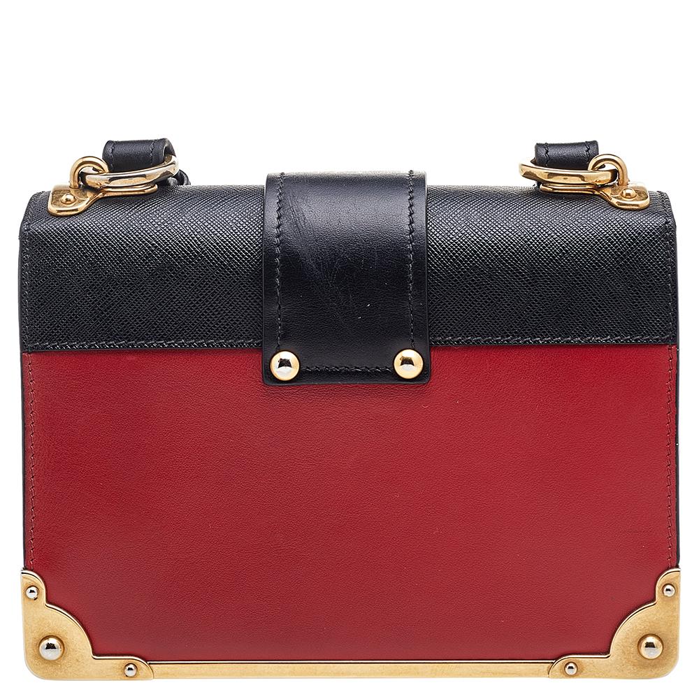 Inspired by valuable books from ancient times, the Cahier by Prada is a best-seller. This shoulder bag is crafted in Italy with black and red leather. It features gold-tone trims that add a touch of contrast. The strap closure with the brand logo