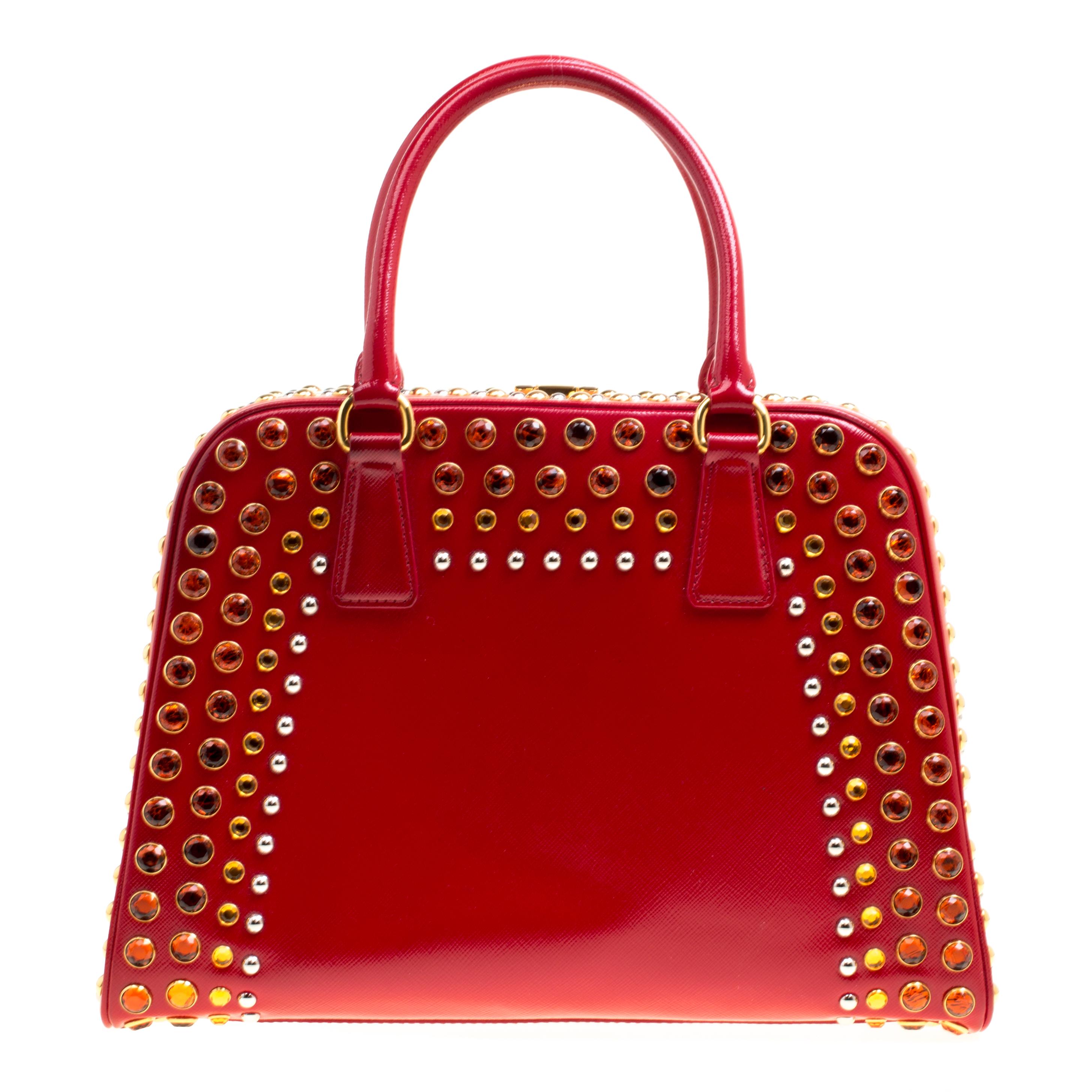 This marvelously designed top handle bag from Prada is the epitome of charm and style. Everything about the bag speaks opulence and a glamorous finish. Sculpted in a pyramid frame style, the bag is crafted from shiny red patent leather with