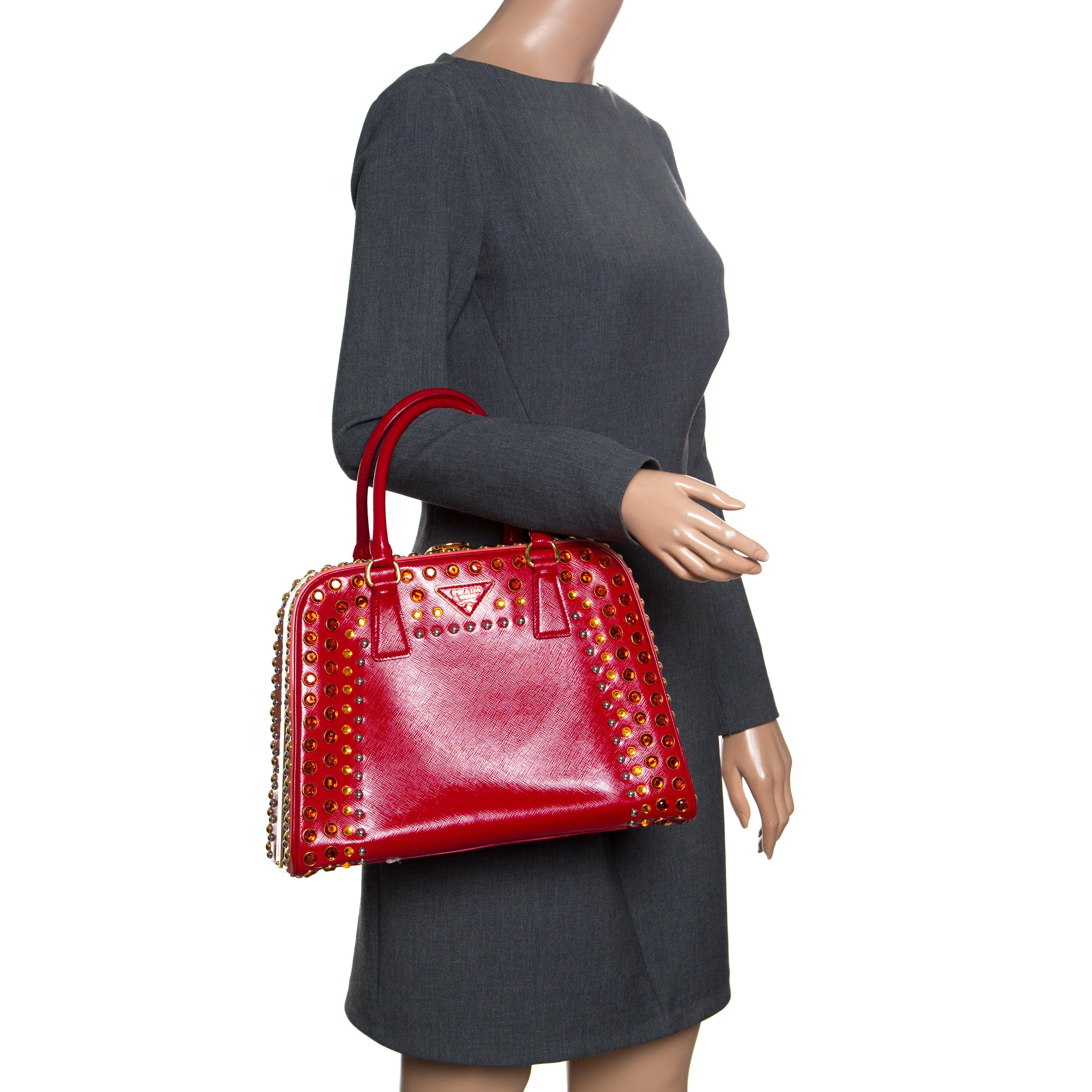 This marvelously designed top handle bag from Prada is the epitome of charm and style. Everything about the bag speaks opulence and a glamorous finish. Sculpted in a pyramid frame style, the bag is crafted from shiny red patent leather with