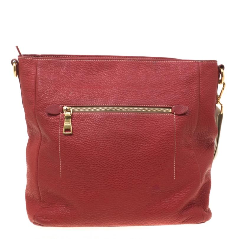 Prada presents an expertly crafted messenger bag. Made from red pebbled leather, the bag features a shoulder strap and zip pockets both at the front and back. The well-sized interior is lined with nylon and secured by a zip closure. The bag is
