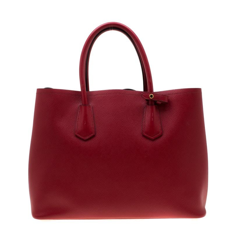 This lovely tote from Prada is crafted from Saffiano Cuir leather and features a vibrant red shade. It flaunts dual round handles, an attached tag, protective metal feet, and a spacious leather-lined interior. Perfect to complement most of your