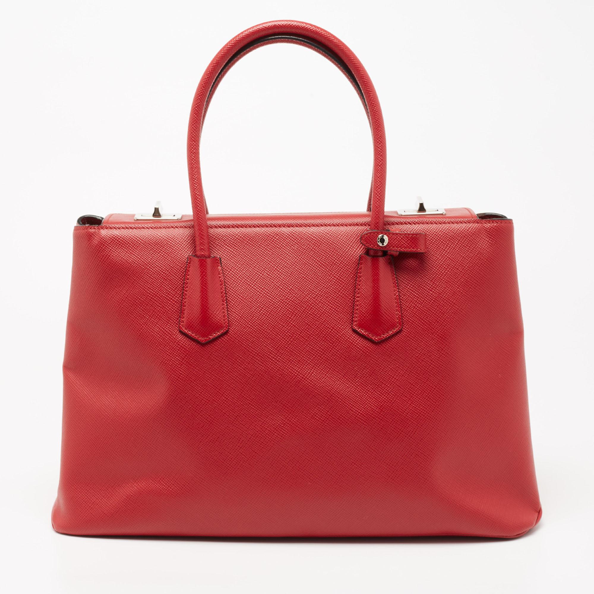 Add effortless style and luxury to your everyday looks with this stunning Prada Twin tote. Crafted in red Saffiano Cuir leather, this bag can store all that you need through the day or for work in its compartments. The bag is equipped with dual
