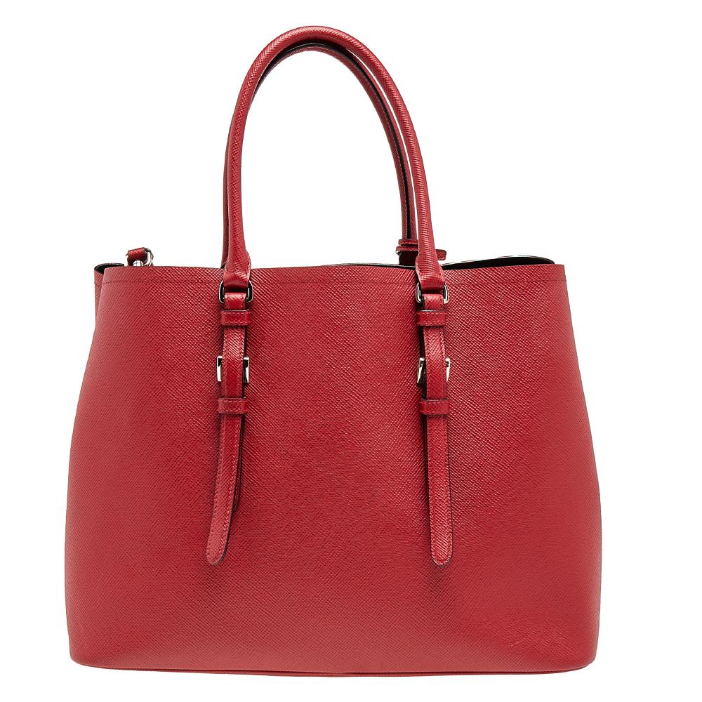This lovely tote from Prada is crafted from Saffiano Cuir leather in a red shade. It flaunts dual handles, a shoulder strap, the brand logo at the front, protective metal feet, and a spacious leather-lined interior with enough space to house all